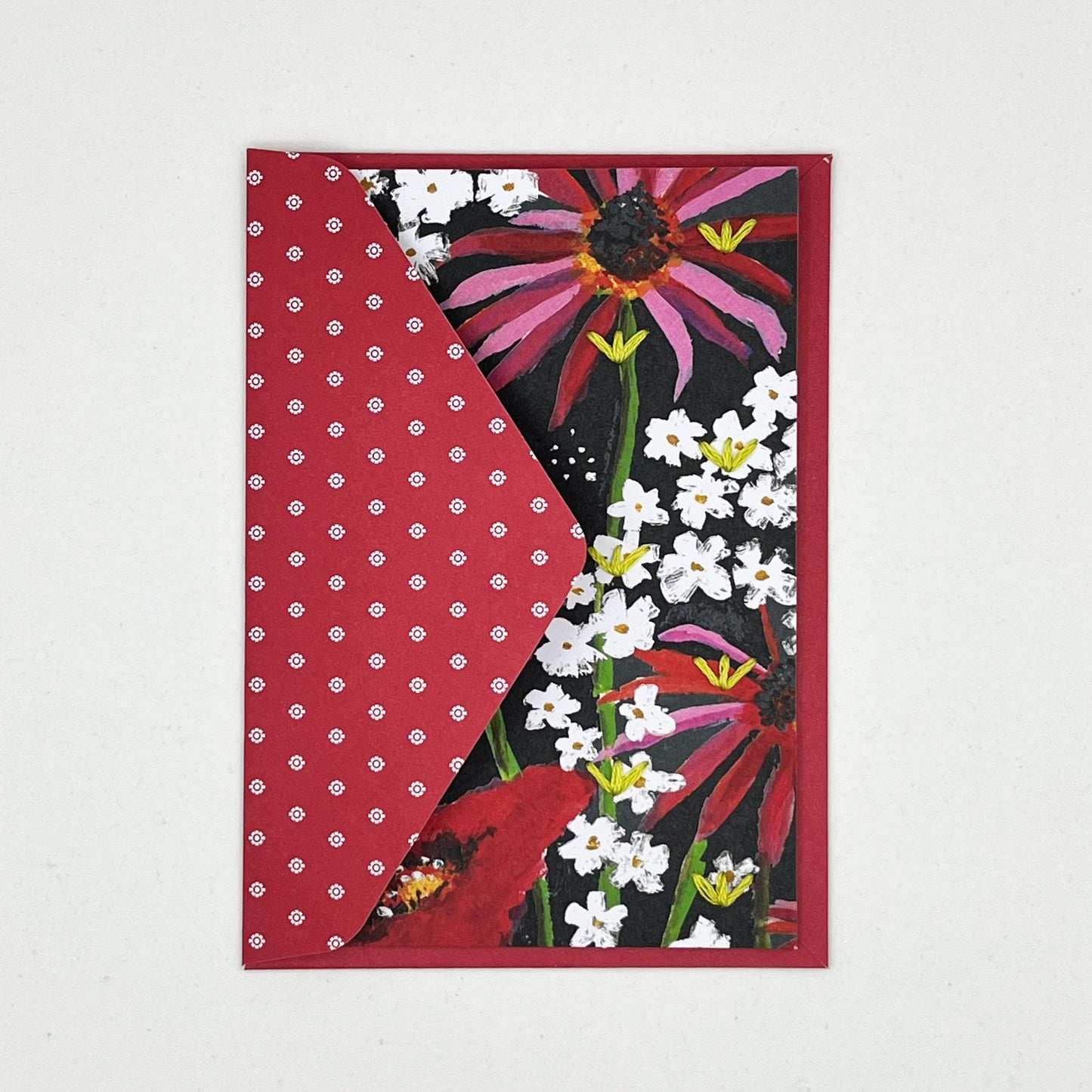 Greeting card tucked into a flap of an envelope. artwork of painted flowers in red pink and white. Chartreuse stitches of sprout shapes in zig zag pattern on right side of card