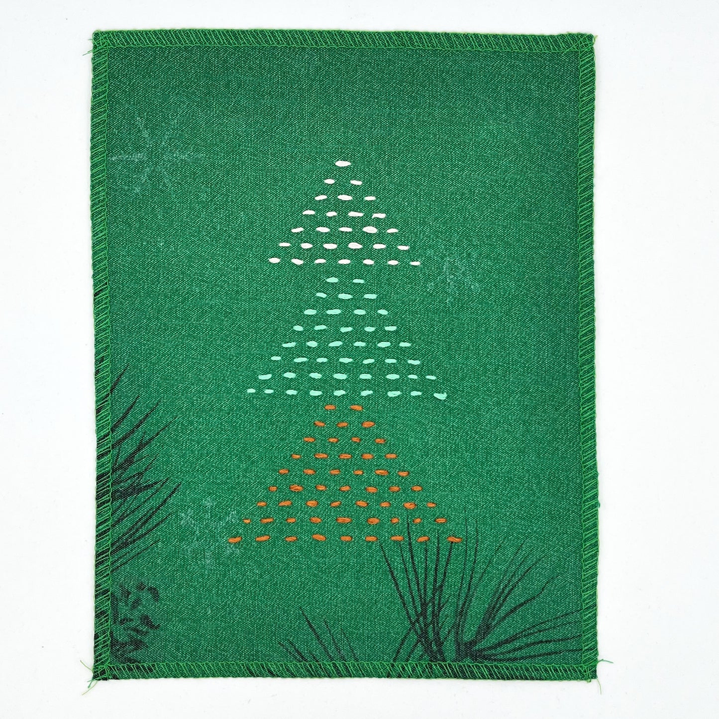 a fabric wall hanging made from bright green fabric with pine branches printed on it, and stitched over with Christmas trees made from three triangles, each triangle made from running stitches in red green and peach, on a white background