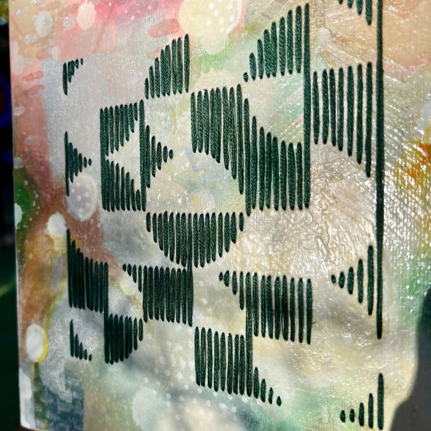 close up angled view of a colorful square painting in a wood frame with an abstract image of divided circles in a grid hand stitched on it in emerald green embroidery floss