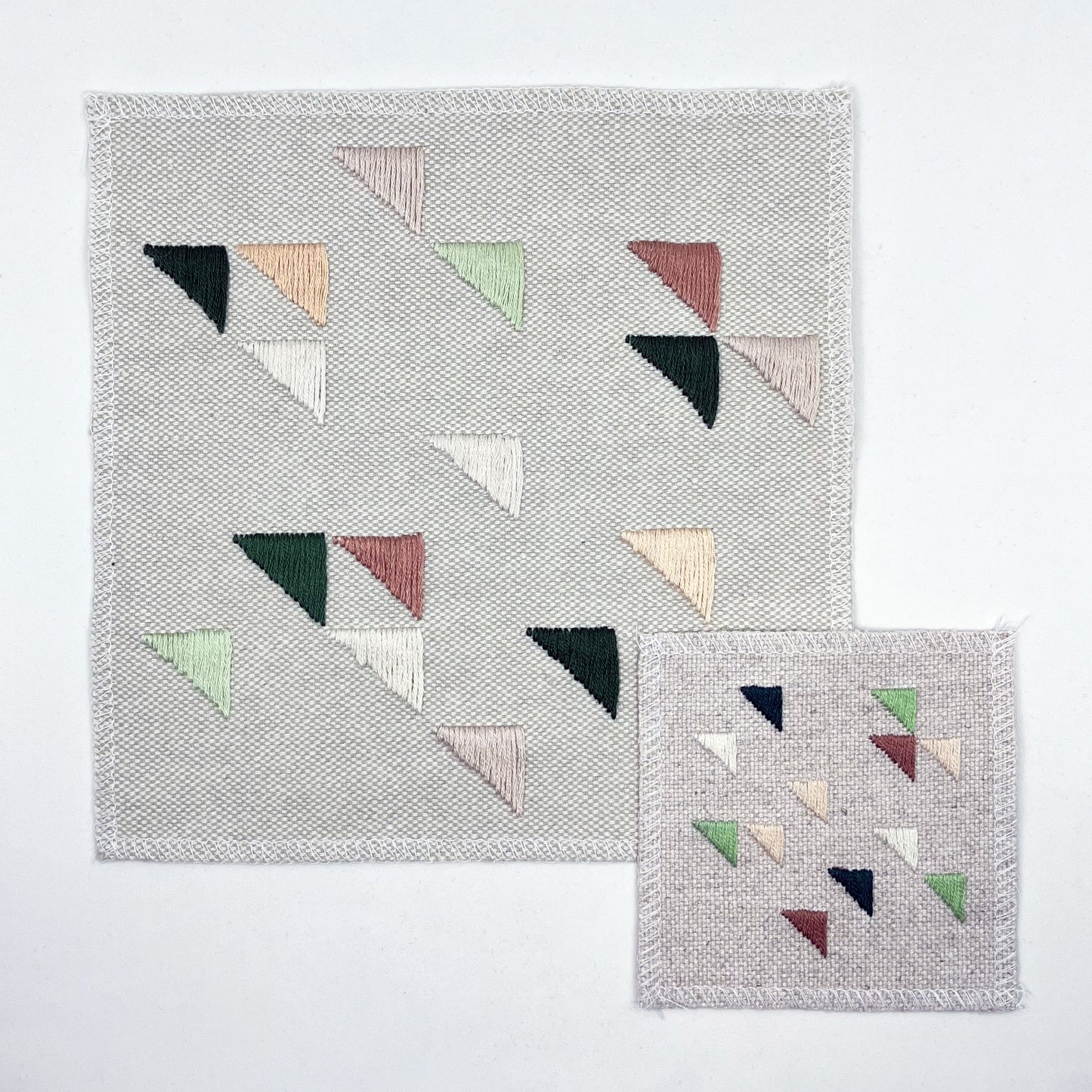 two square natural colored patches in different sizes embroidered with randomly placed triangles in peaches, mauves and greens, on a white background