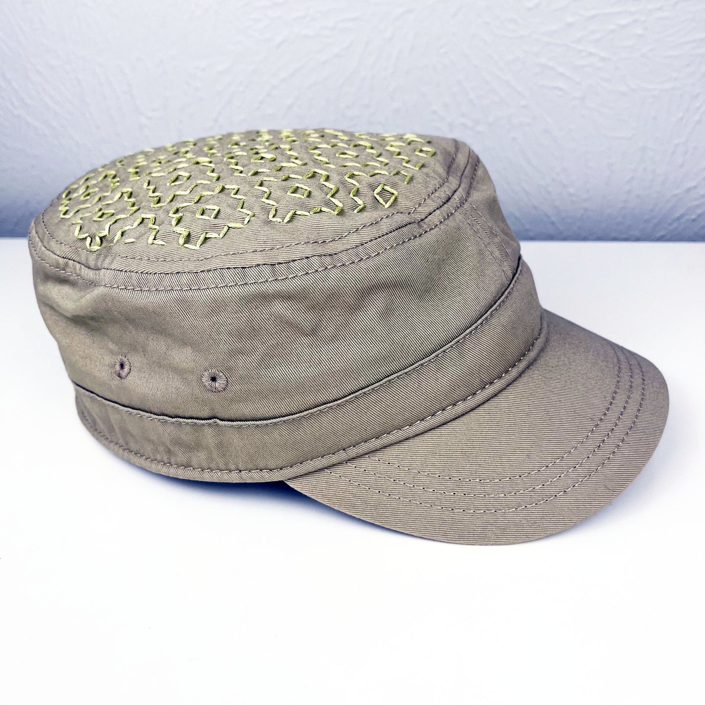 tan cadet hat with persimmon sashiko pattern stitched in chartreuse thread on the top, sitting on a white dresser