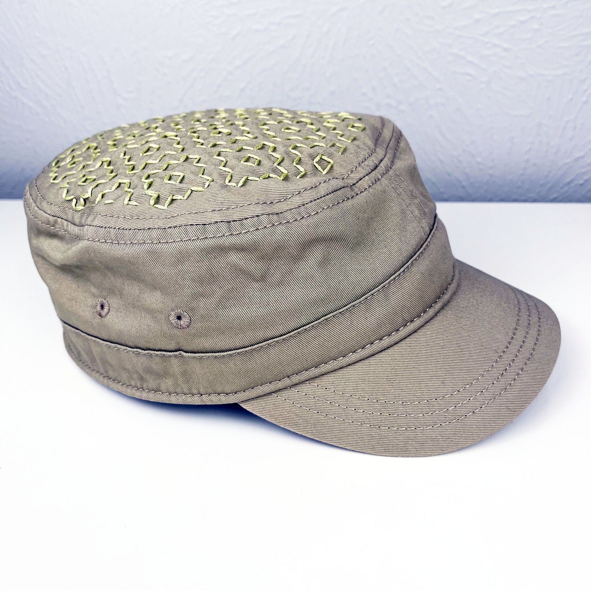 tan cadet hat with persimmon sashiko pattern stitched in chartreuse thread on the top, sitting on a white dresser