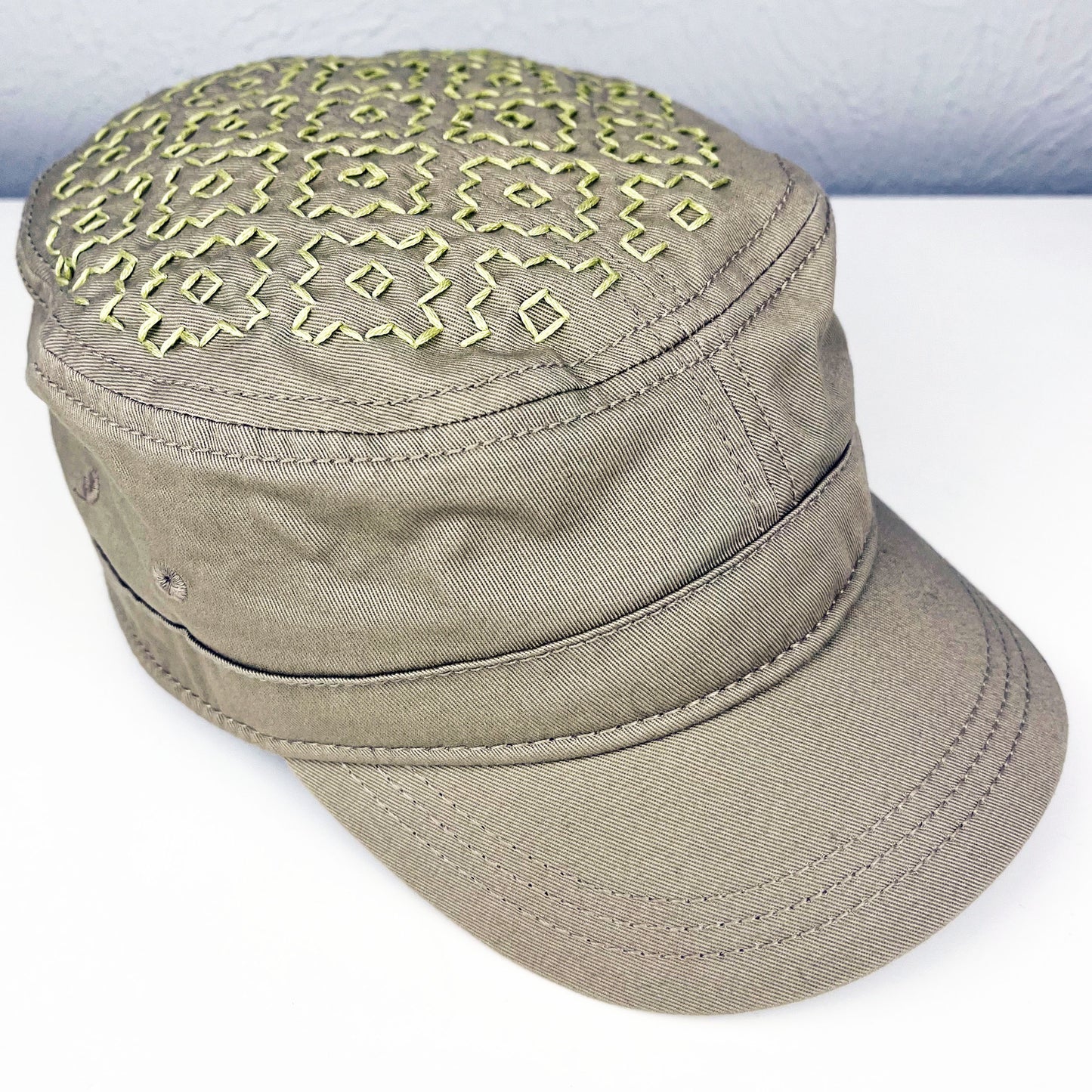 tan cadet hat with persimmon sashiko pattern stitched in chartreuse thread on the top, sitting on a dresser with a plant vine and dried flowers around it