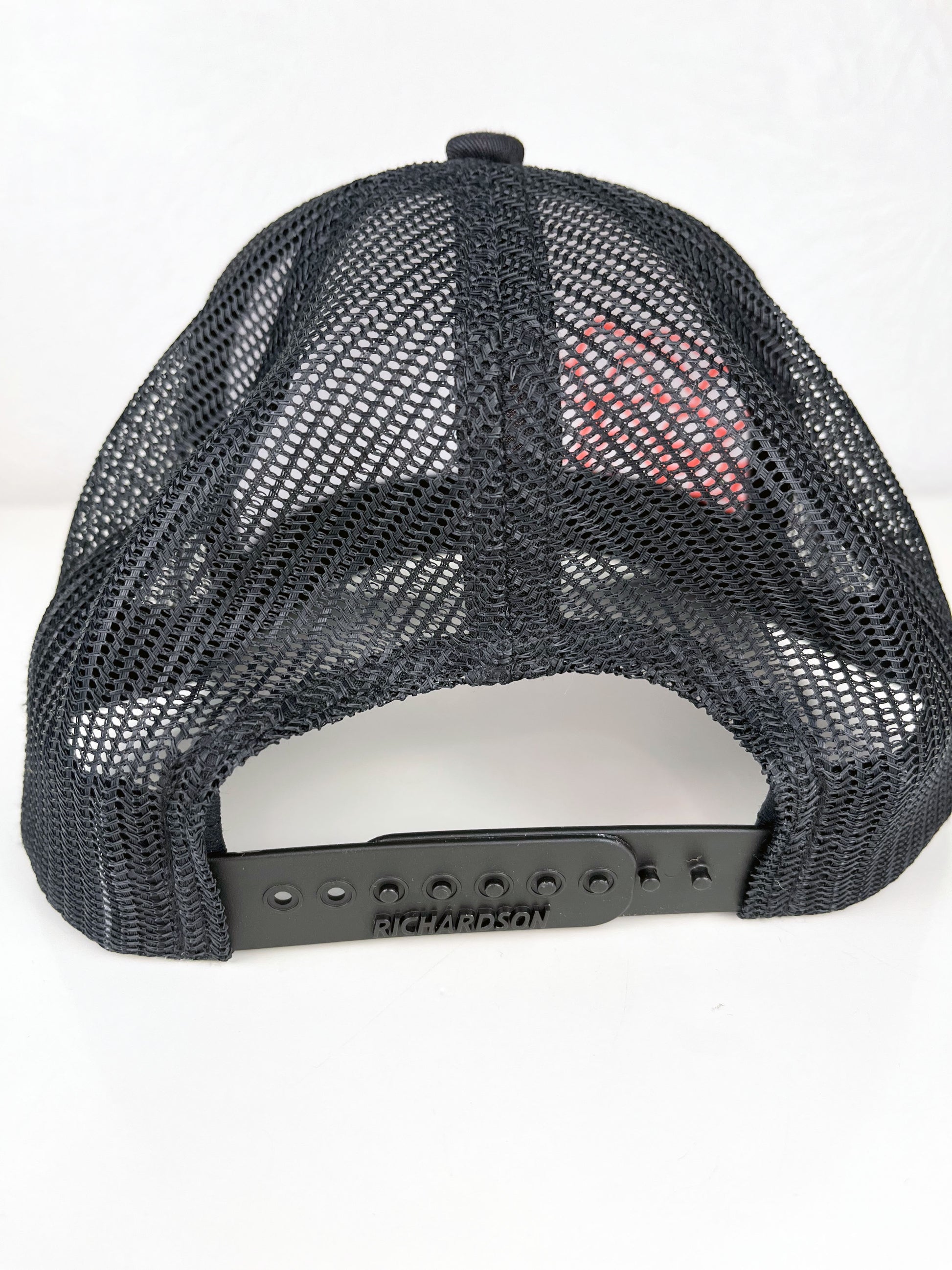 back view of black mesh hat with neon pink outline of a peony hand embroidered to the front, sitting on a white dresser