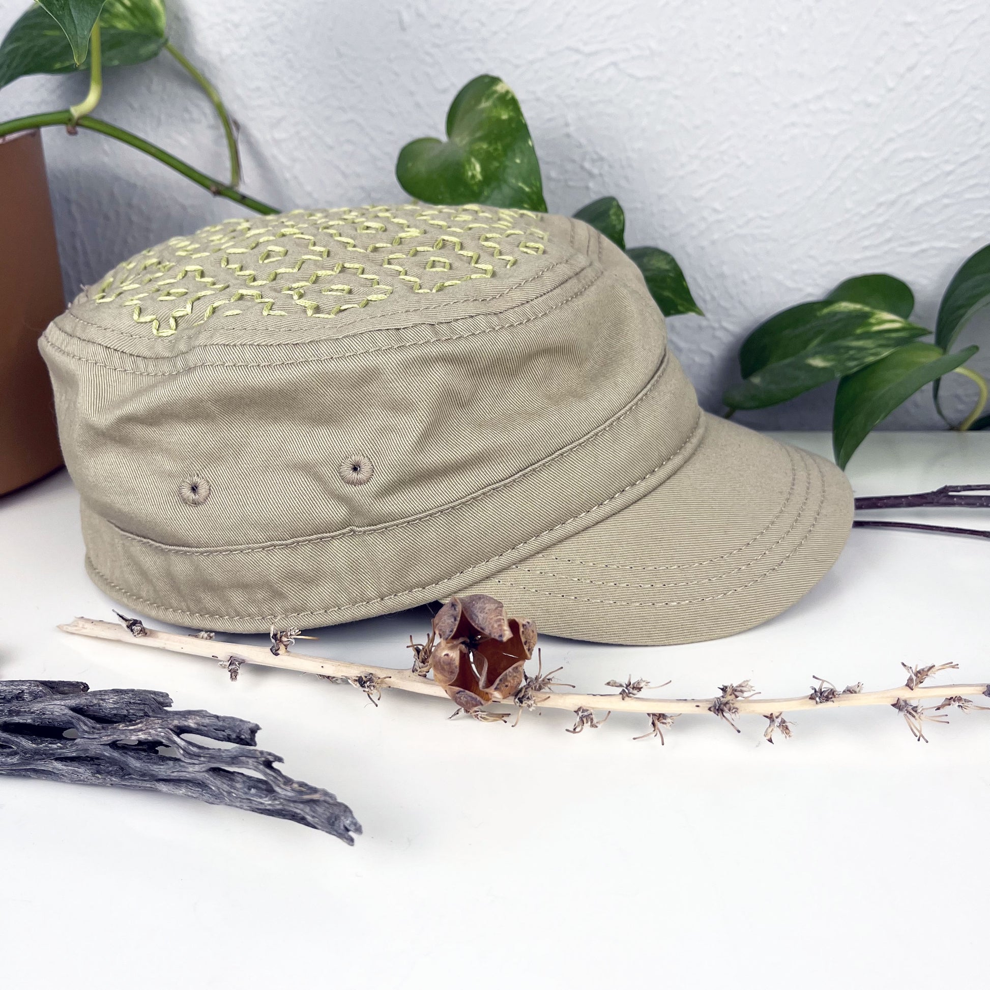 tan cadet hat with persimmon sashiko pattern stitched in chartreuse thread on the top, sitting on a dresser with a plant vine and dried flowers around it