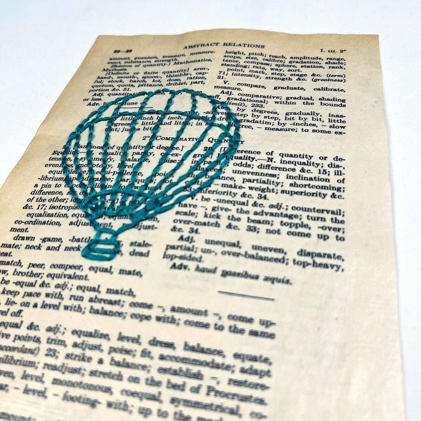 a close up angled view of a vintage thesaurus page, hand stitched over with an outline of a hot air balloon in teal thread