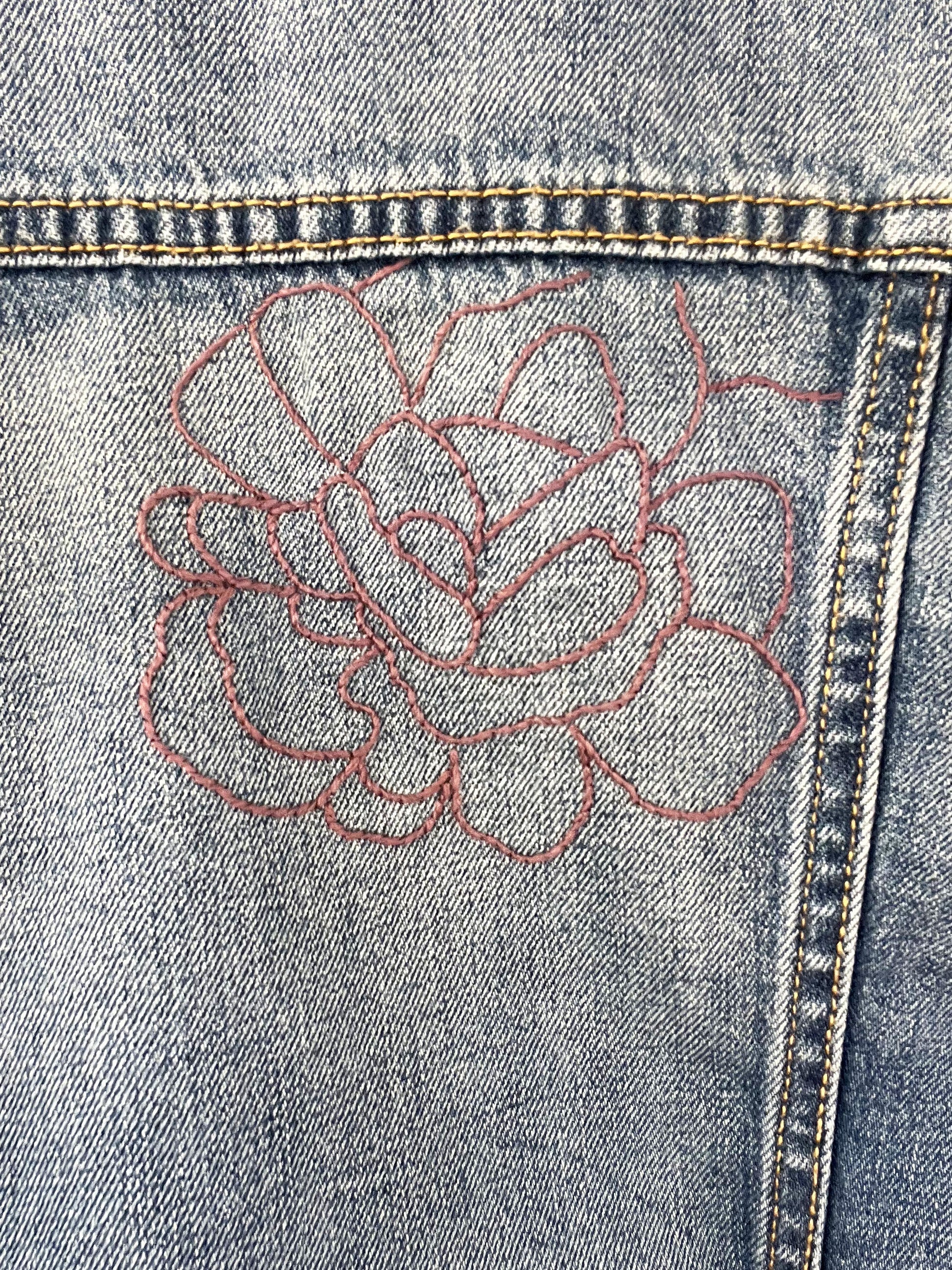 close up view of a denim jacket with an outline of a large peony in purple