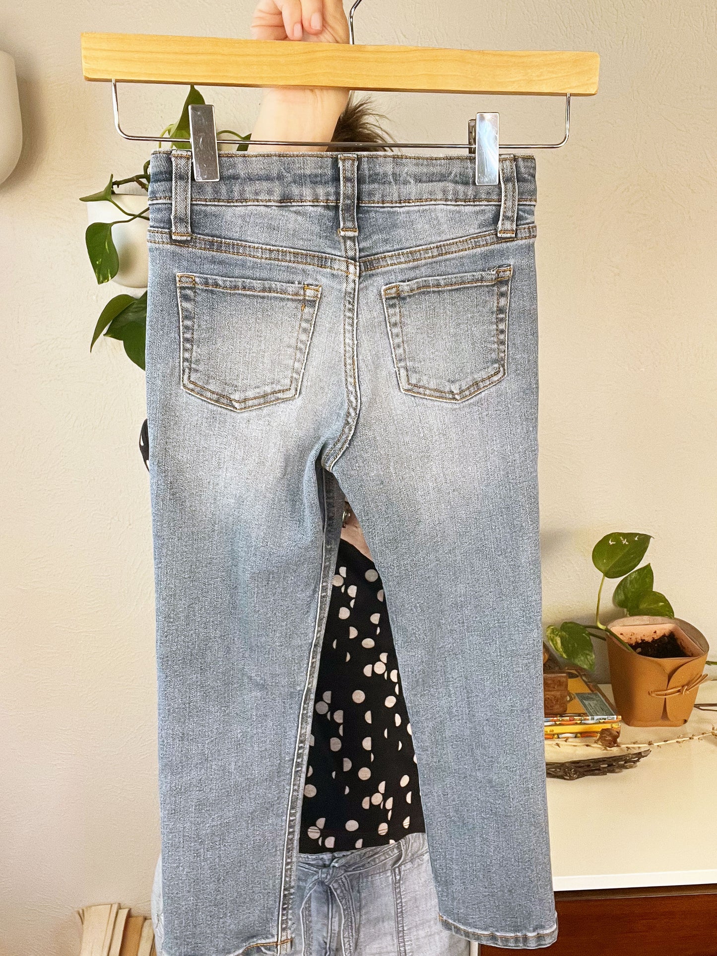 back view of blue jeans front pocket with hand embroidered flowers in greens and pinks, using chainstitch, stem stitch, and french knots, being held up on a hanger