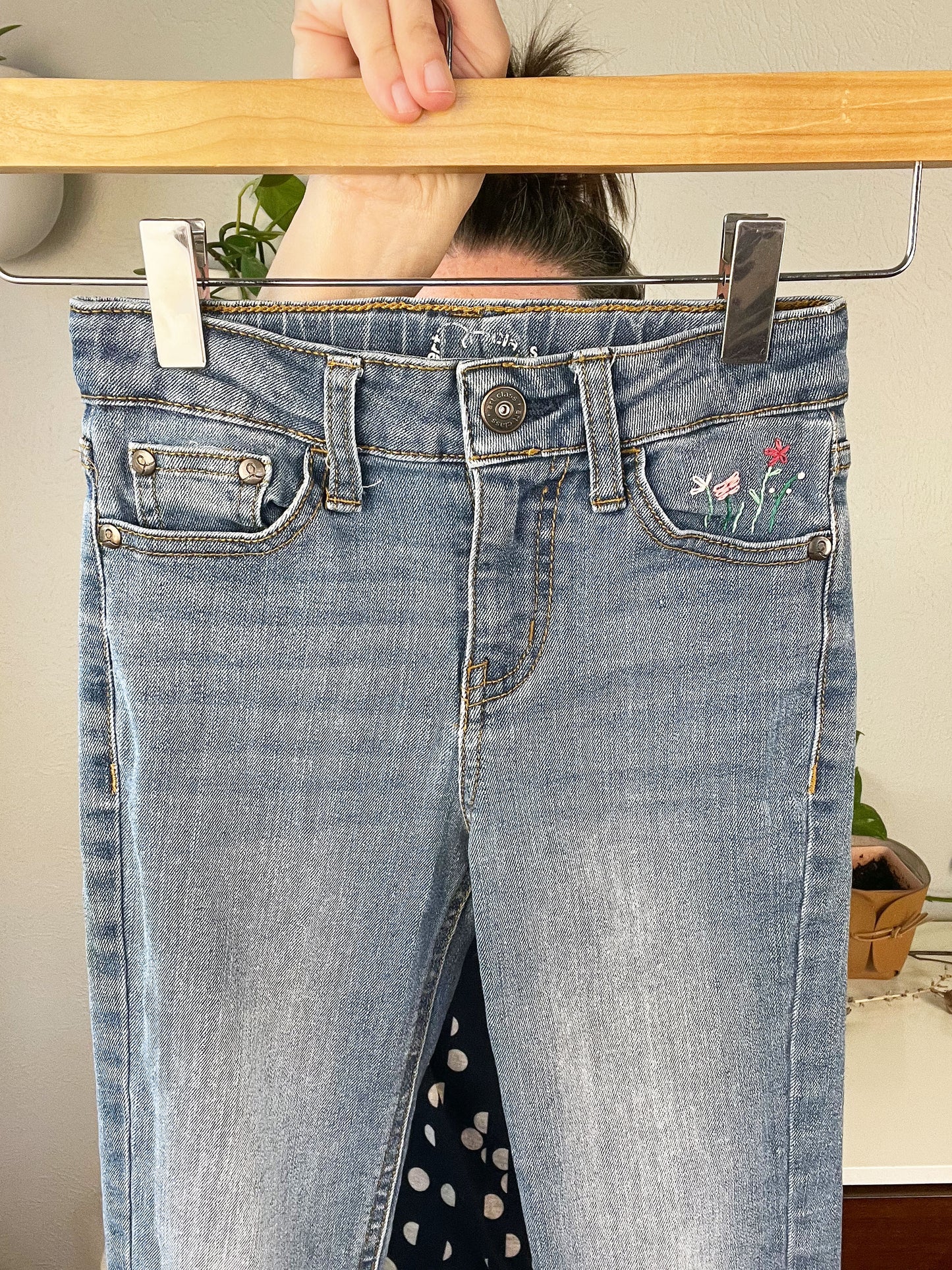 front view of blue jeans front pocket with hand embroidered flowers in greens and pinks, using chainstitch, stem stitch, and french knots