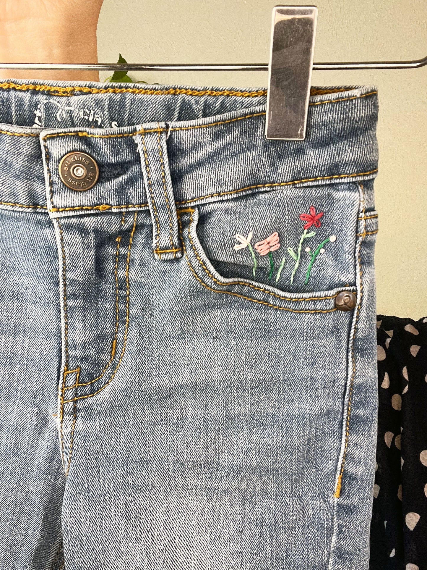 close up view of blue jeans front pocket with hand embroidered flowers in greens and pinks, using chainstitch, stem stitch, and french knots