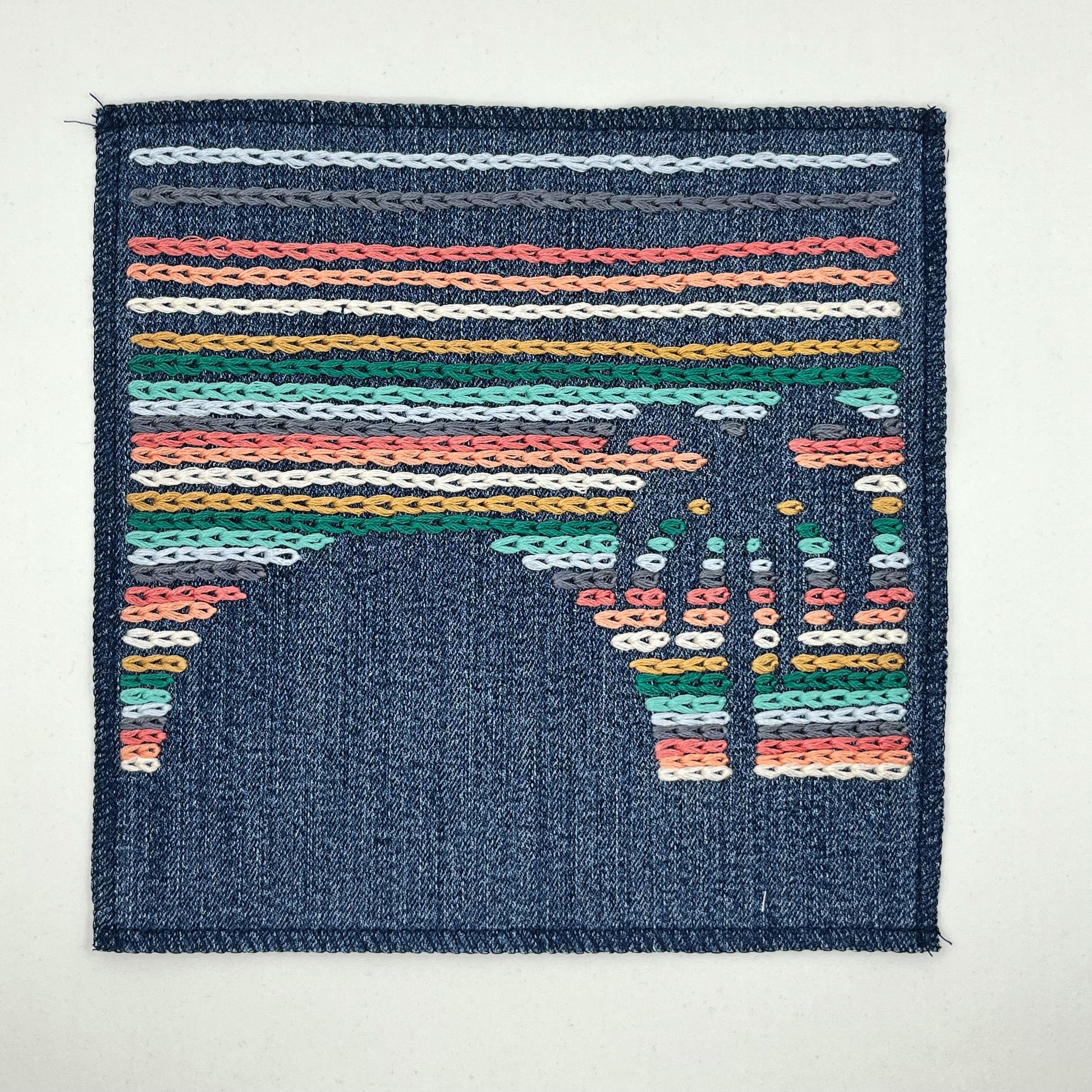 a large square denim patch, hand stitched with rows of chainstitch, with negative space showing the shapes of a palm tree next to a setting sun, with peach, coral, grey, light blue, seafoam green and mustard colored thread, on a white background