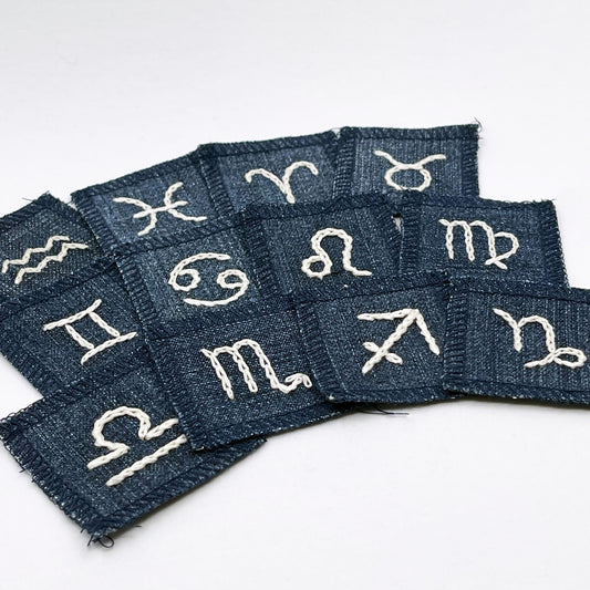 a group of small square denim patches with different zodiac symbols chainstitched onto each one in off white embroidery floss