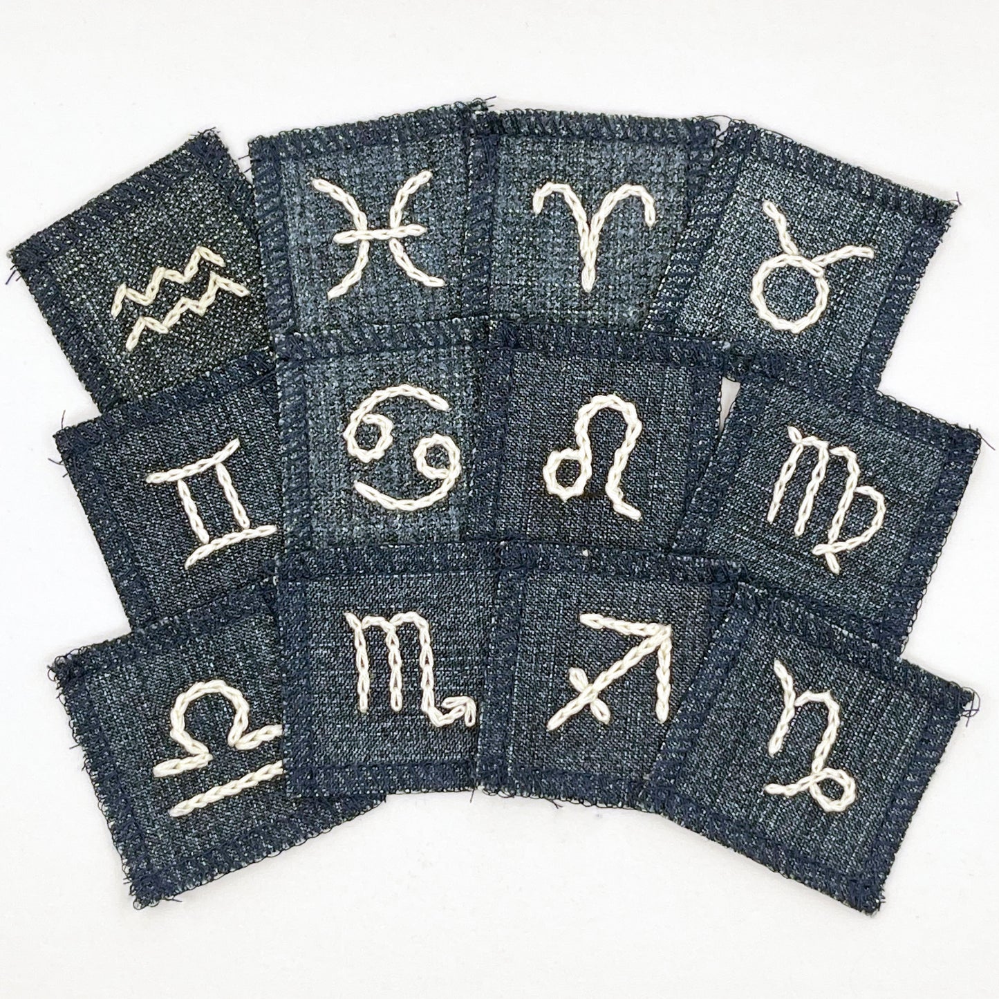a group of small square denim patches with different zodiac symbols chainstitched onto each one in off white embroidery floss