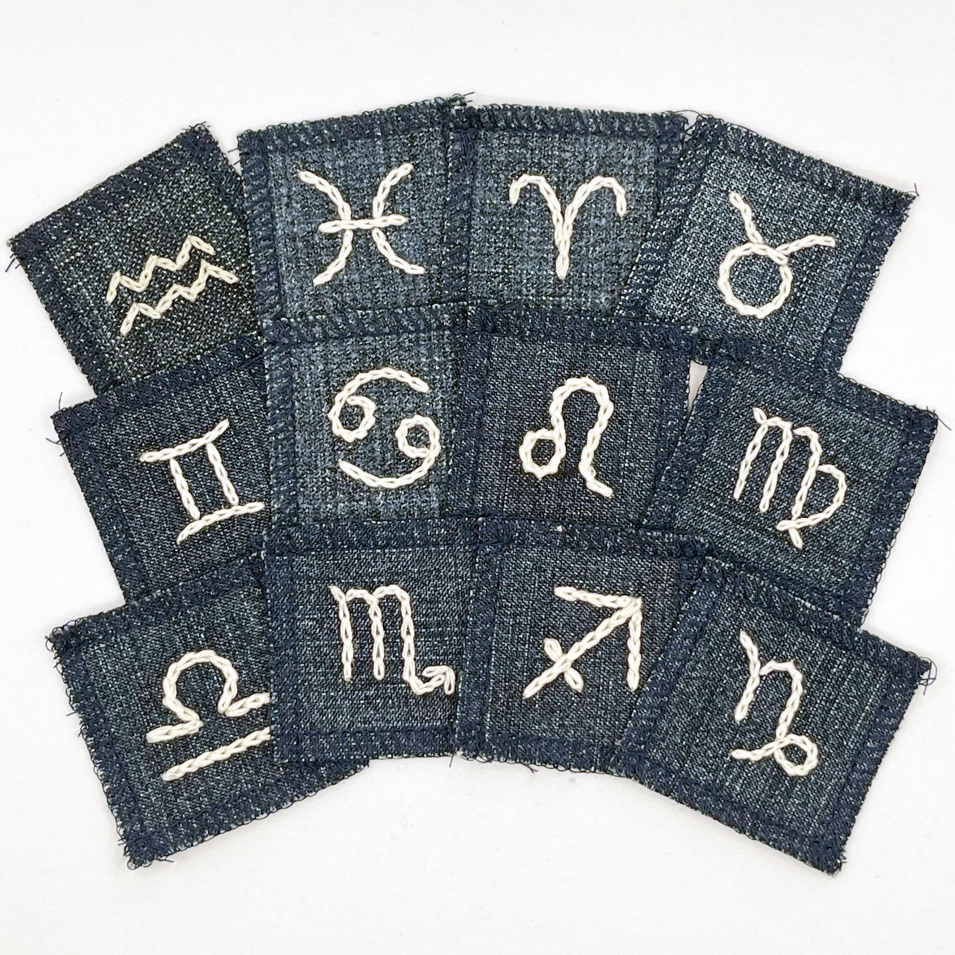 a group of small square denim patches with different zodiac symbols chainstitched onto each one in off white embroidery floss