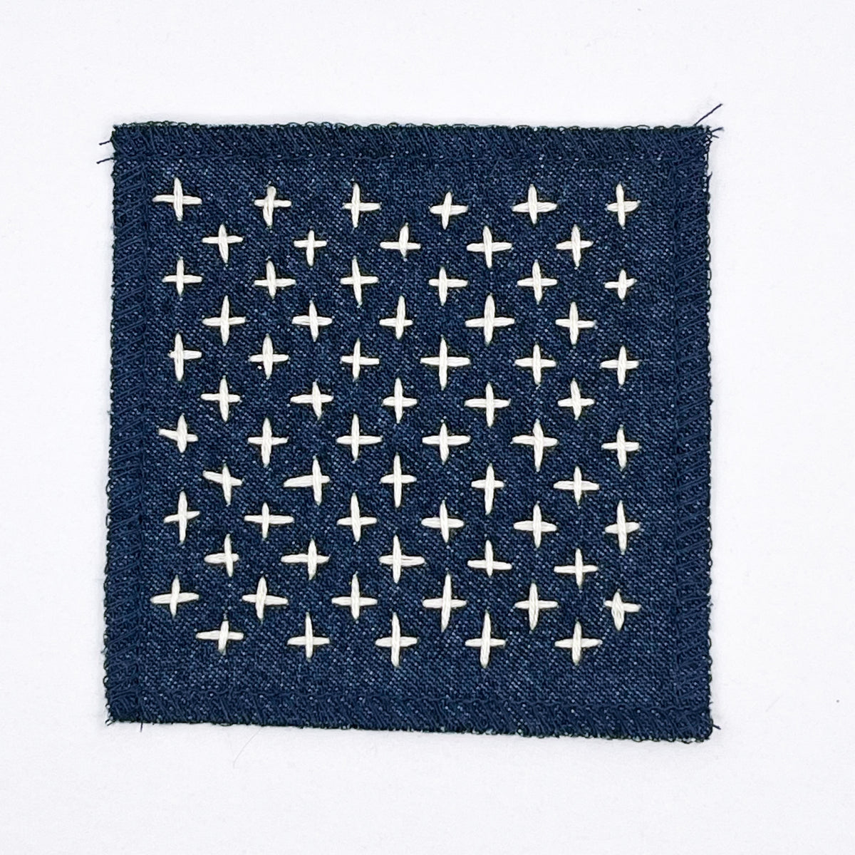 A square denim patch of with and embroidered rows of ivory plus signs, displayed on a clean white background.