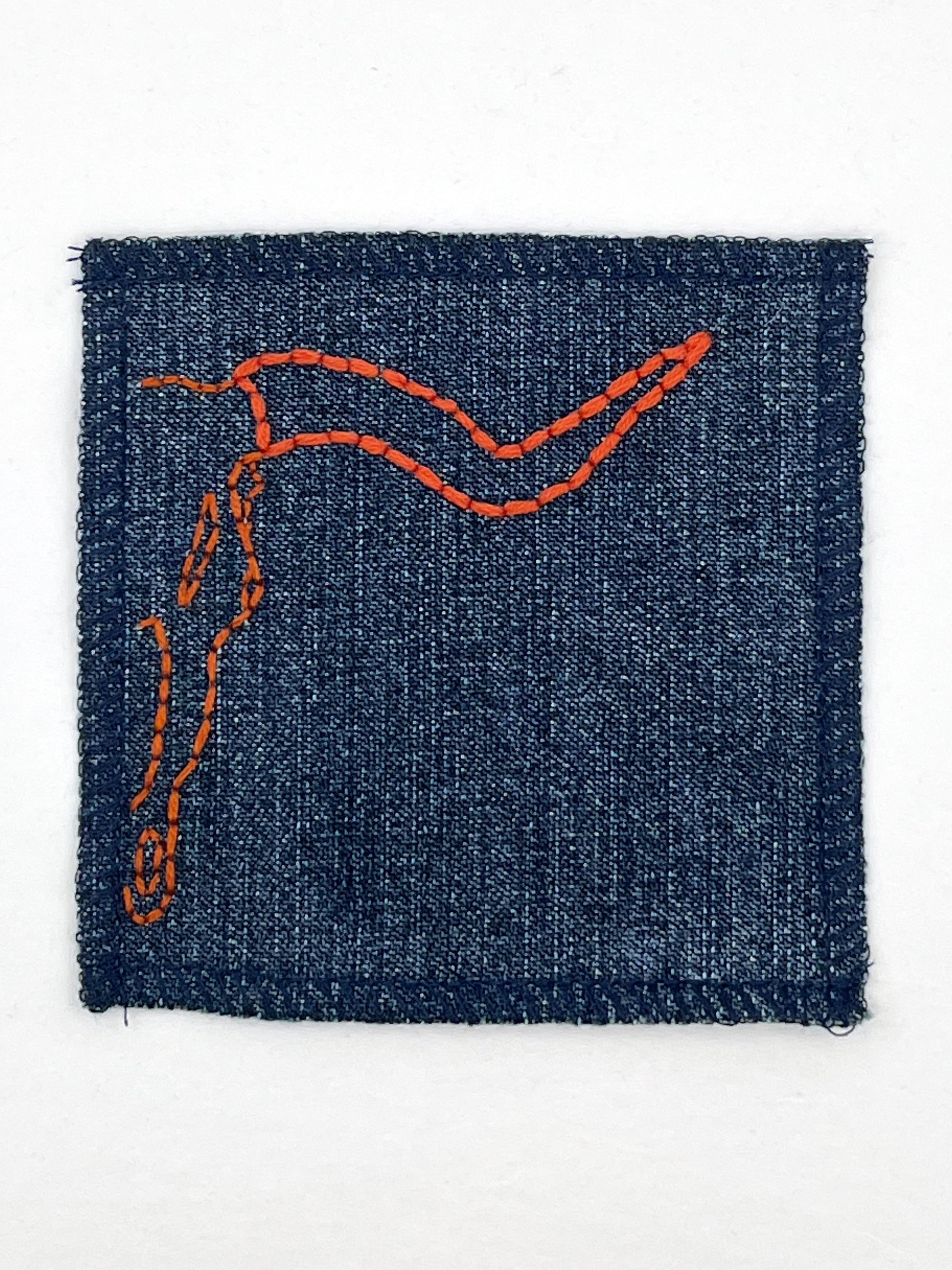 close up view of a square denim patch with overlocked edges, with the right side of a longhorn skull hand embroidered on it. in rust thread with backstitch and french knots, on a white background