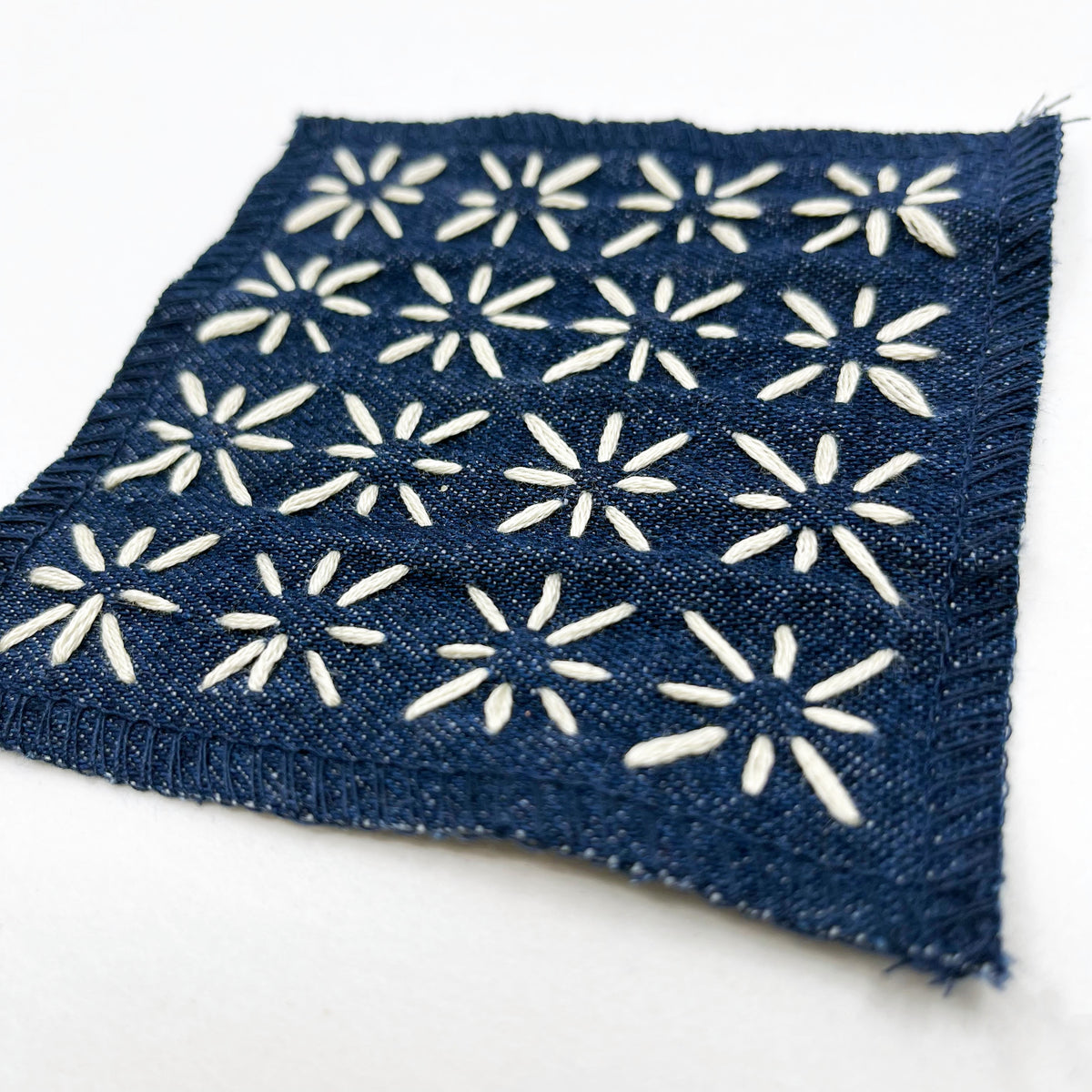 A square denim patch of with ivory star hand embroidery, displayed on a clean white background.