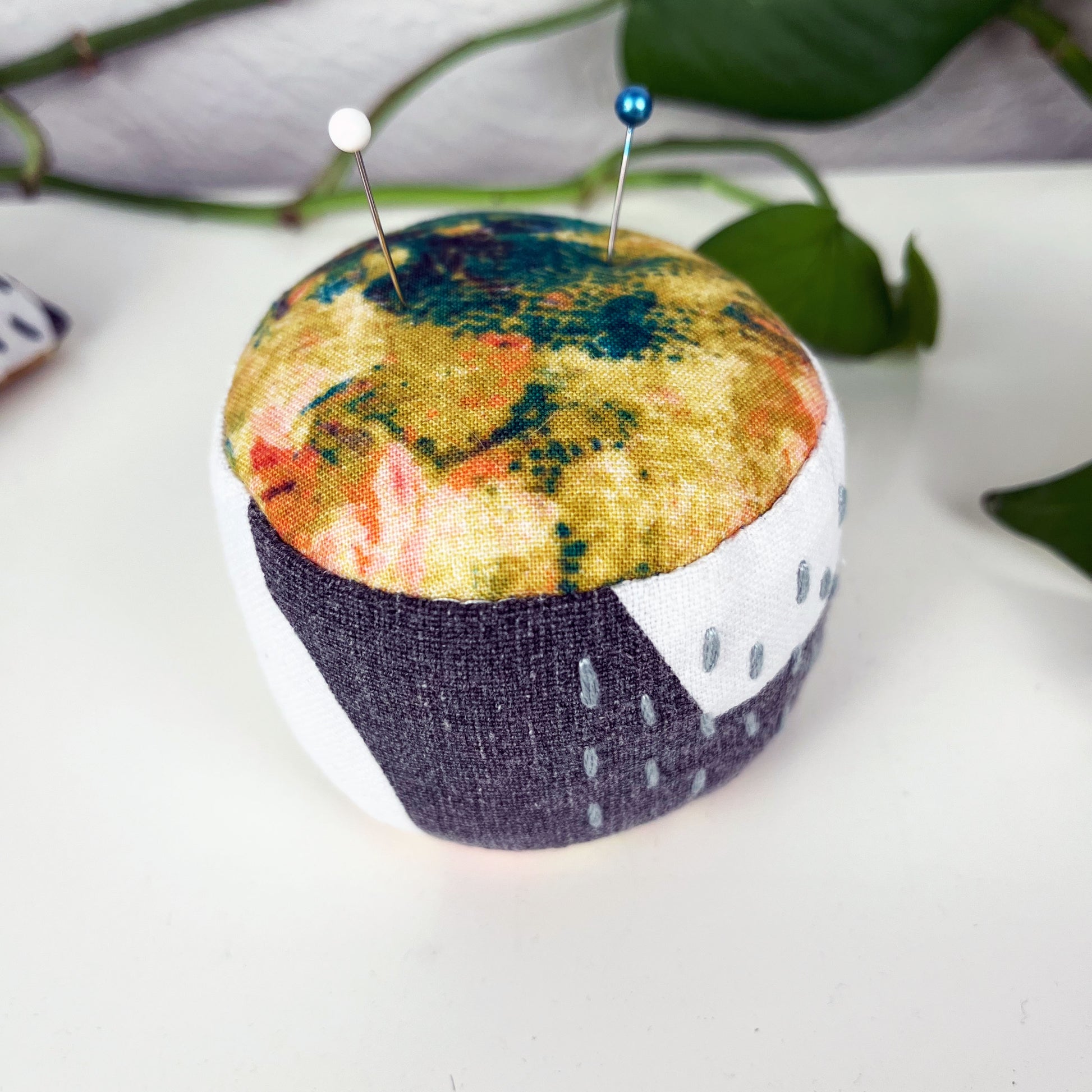 a round pincushion made from multi colored and black and white fabric with contrasting sashiko stitches on the sides 