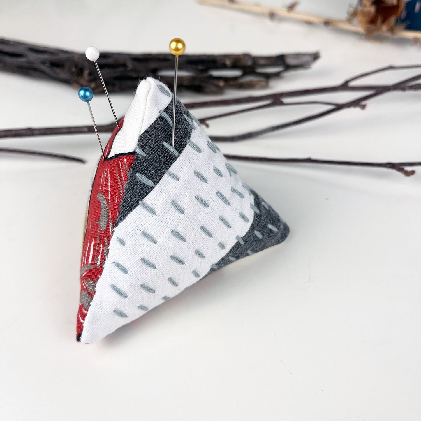 a pyramid pincushion made from floral and black and white fabric with contrasting sashiko stitches on a white counter 