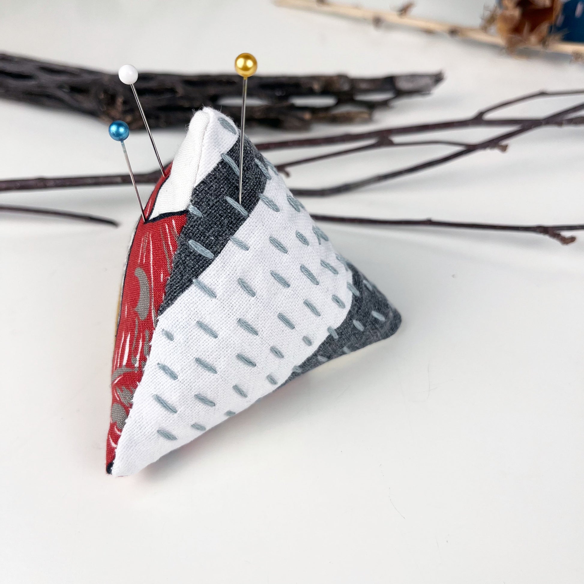 a pyramid pincushion made from floral and black and white fabric with contrasting sashiko stitches on a white counter 
