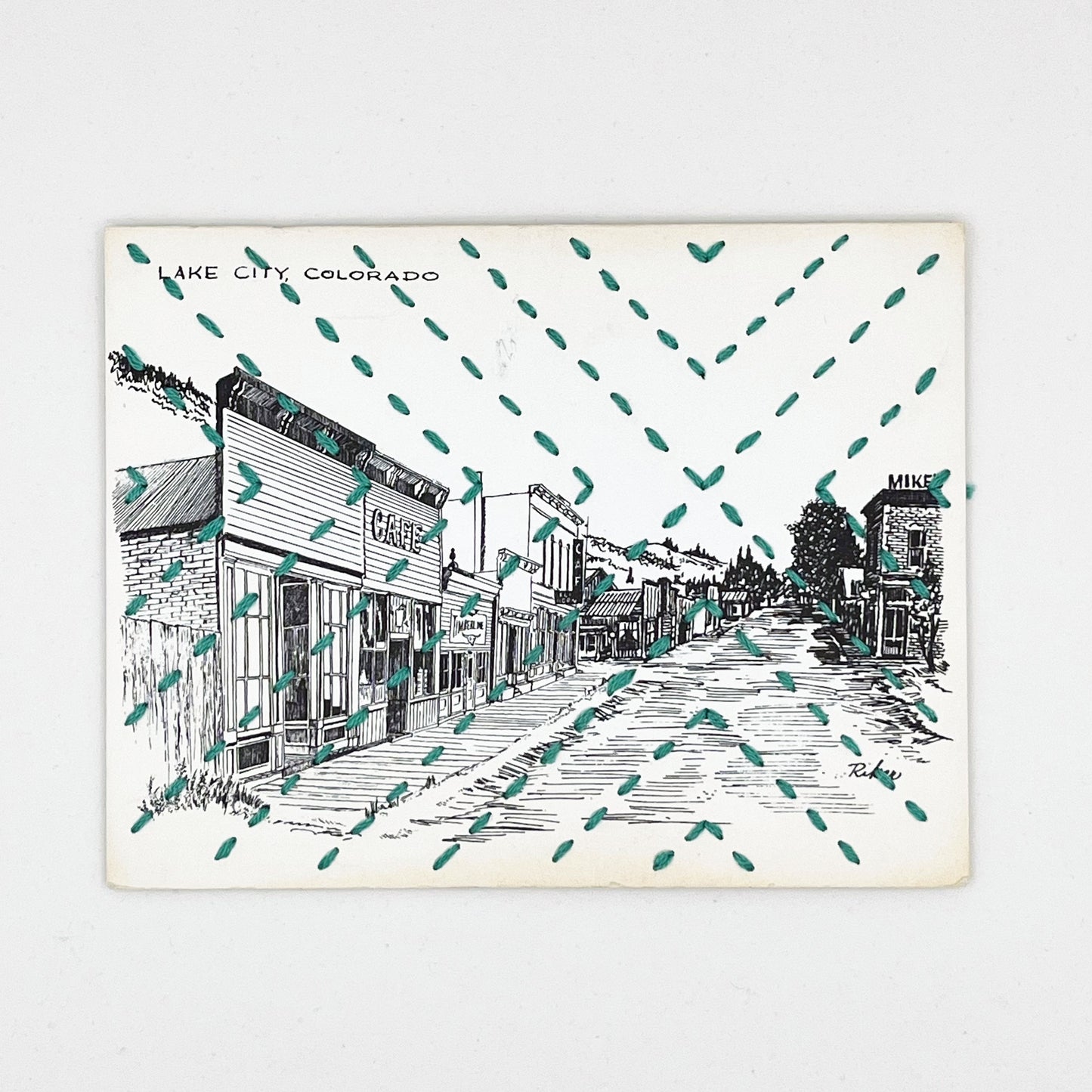 a vintage postcard with a line drawing of Lake City Colorado, hand stitched with a radiating X in green floss