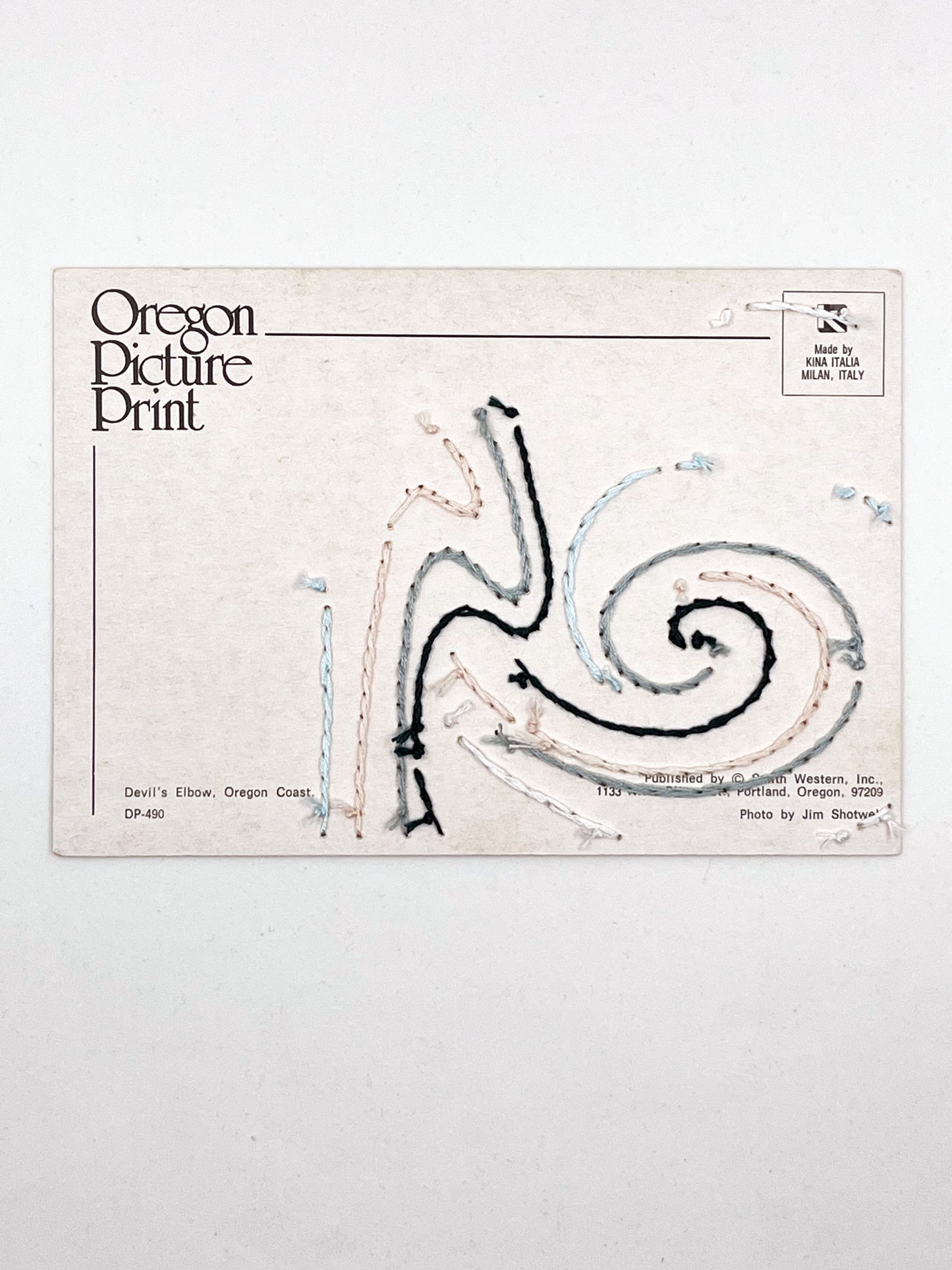 backside of a vintage postcard of the Oregon coast hand embroidered with swirls of forest green peach and grey in the sky