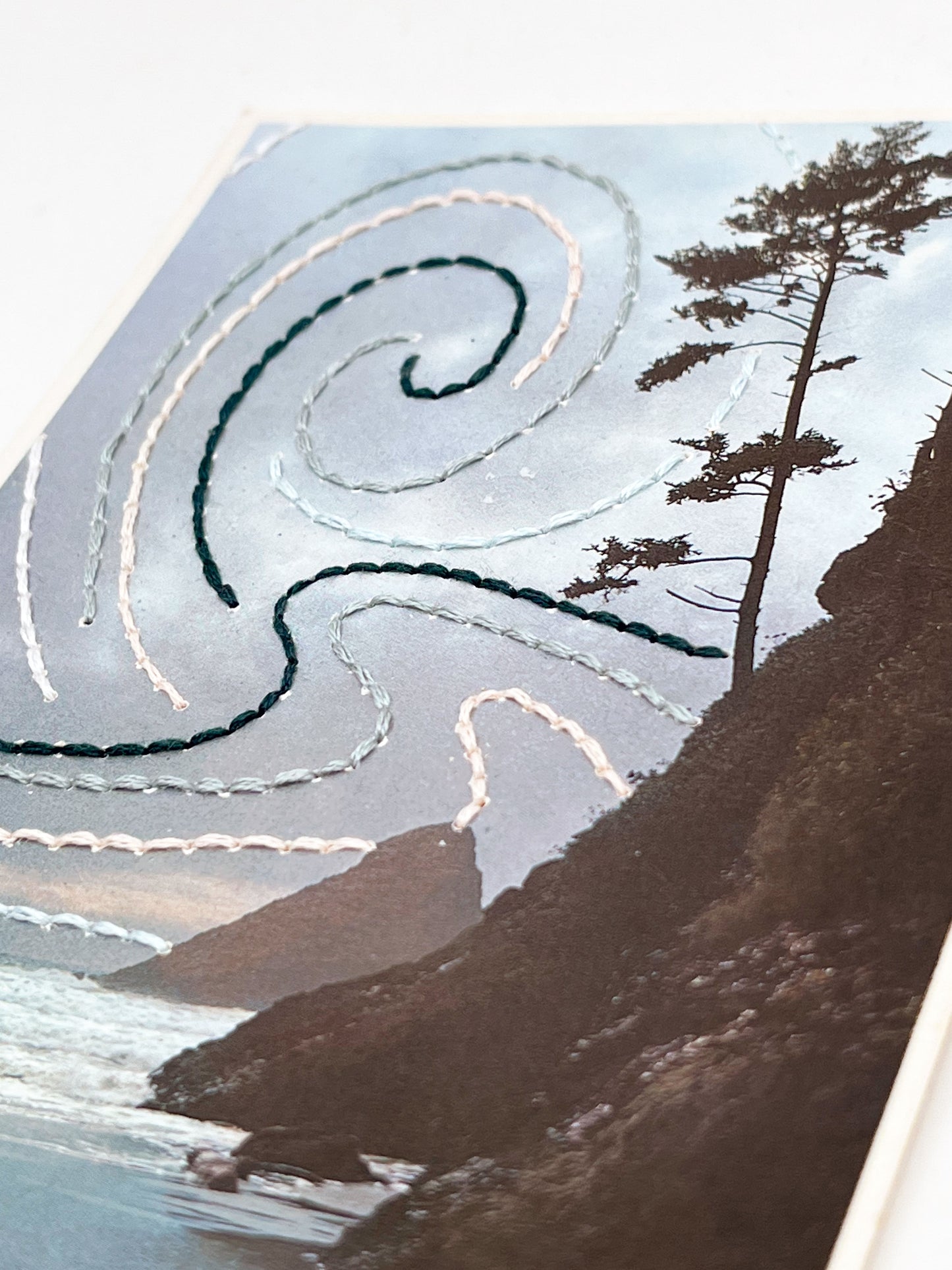 vintage postcard of the Oregon coast hand embroidered with swirls of forest green peach and grey in the sky