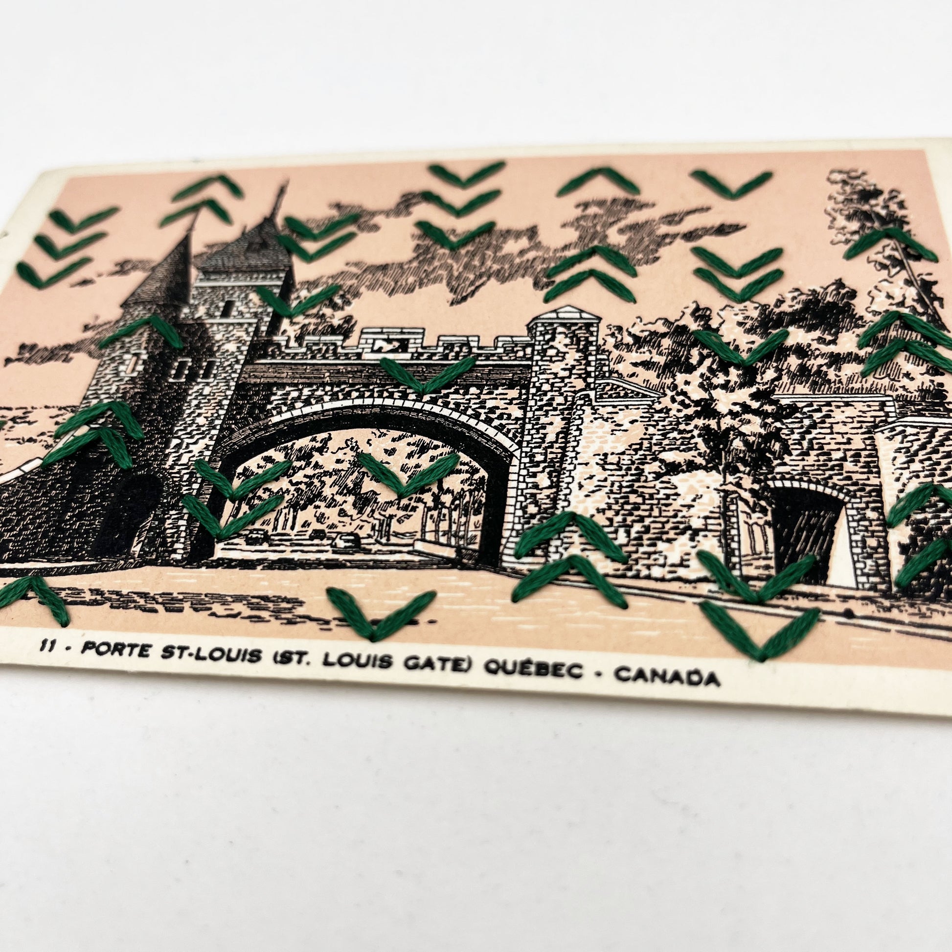 a peach colored vintage postcard of a drawing of St Louis Gate in Quebec, with a pattern of rows of irregularly placed small chevrons hand stitched over it in pine green floss
