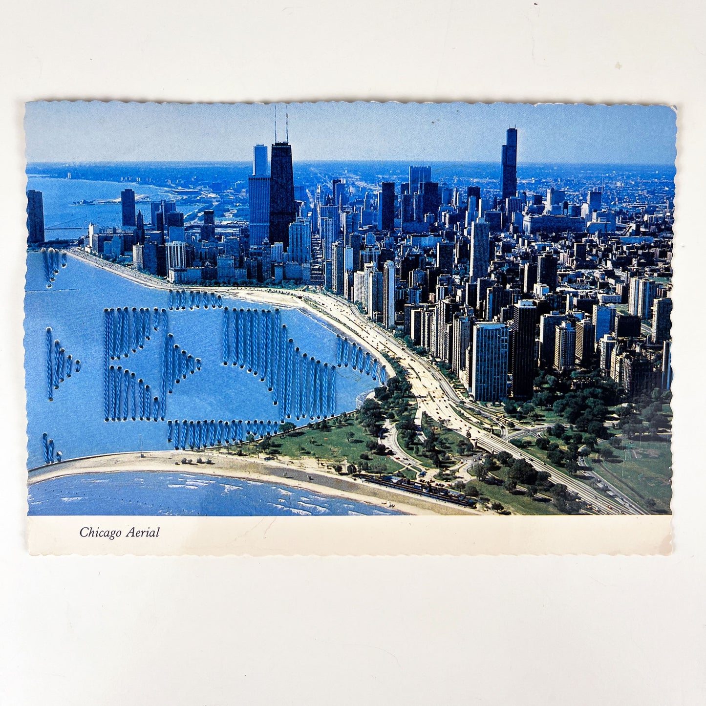 an old postcard of the Chicago skyline along Lake Michigan, with part of the lake hand embroidered over with an abstract partial circle design in blue