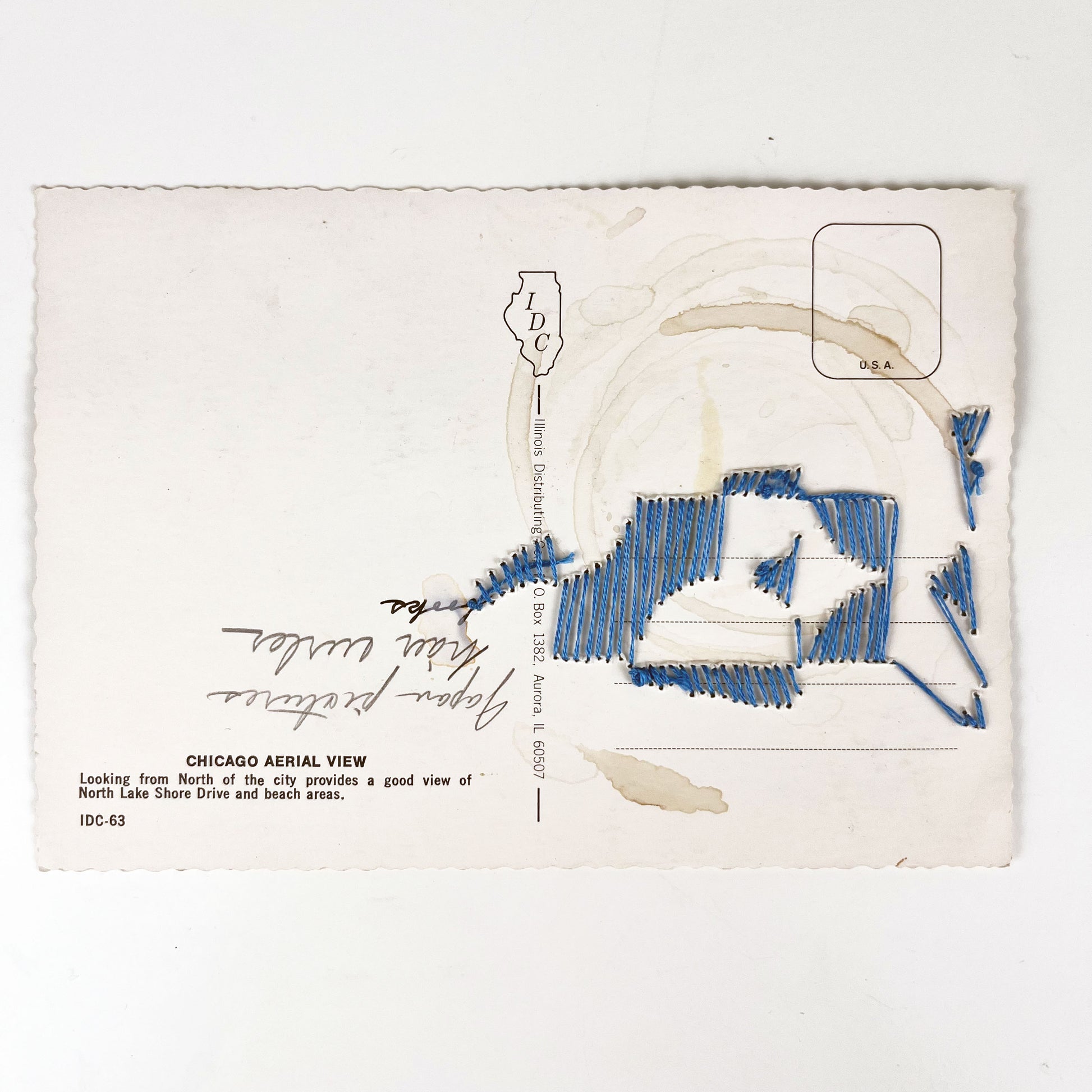 back side of a postcard with backside of stitched pattern showing, the postcard has coffee ring stains and a handwritten list on it