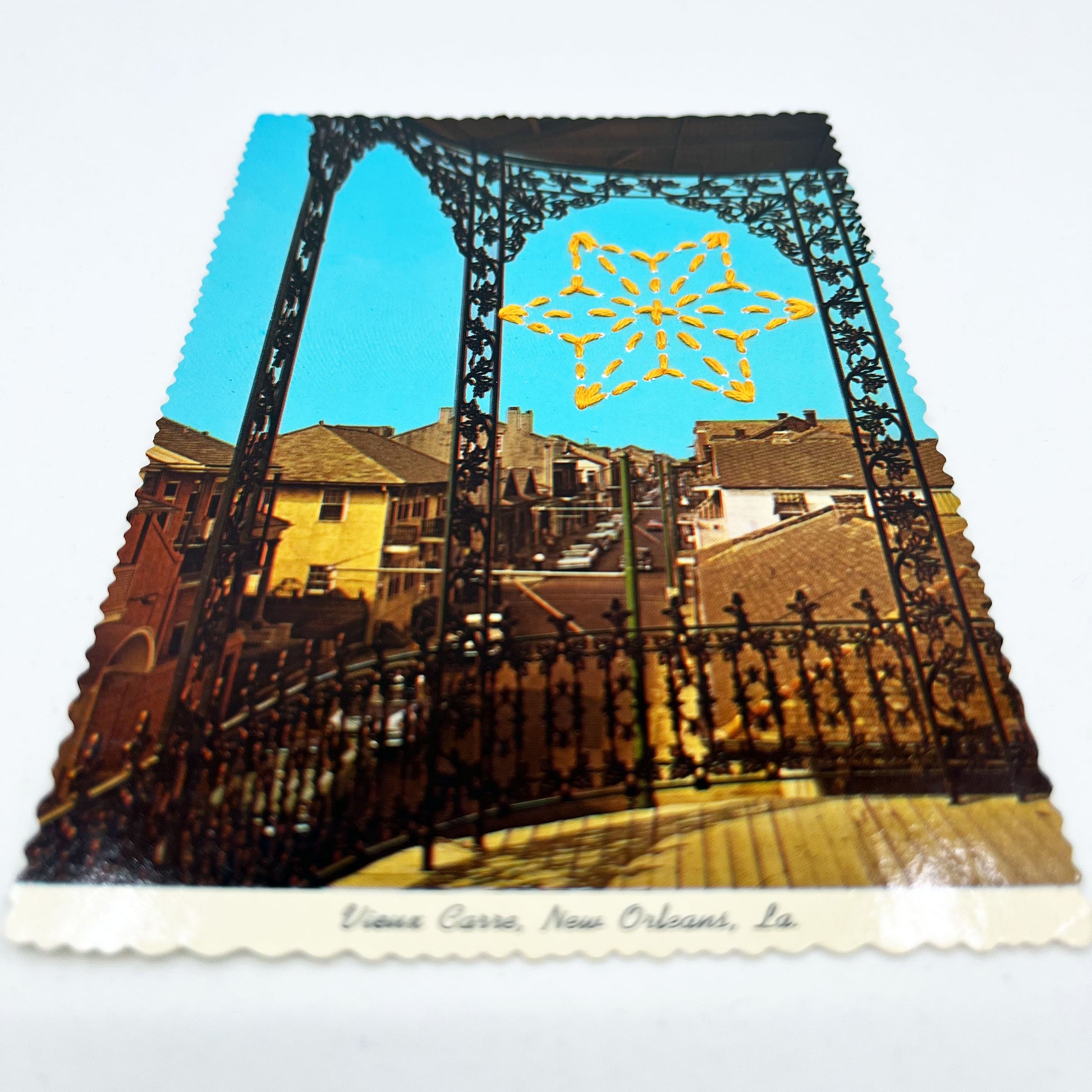 a vintage postcard looking off a wrought iron patio in New Orleans, with a yellow hand stitched sashiko star in the bright blue sky