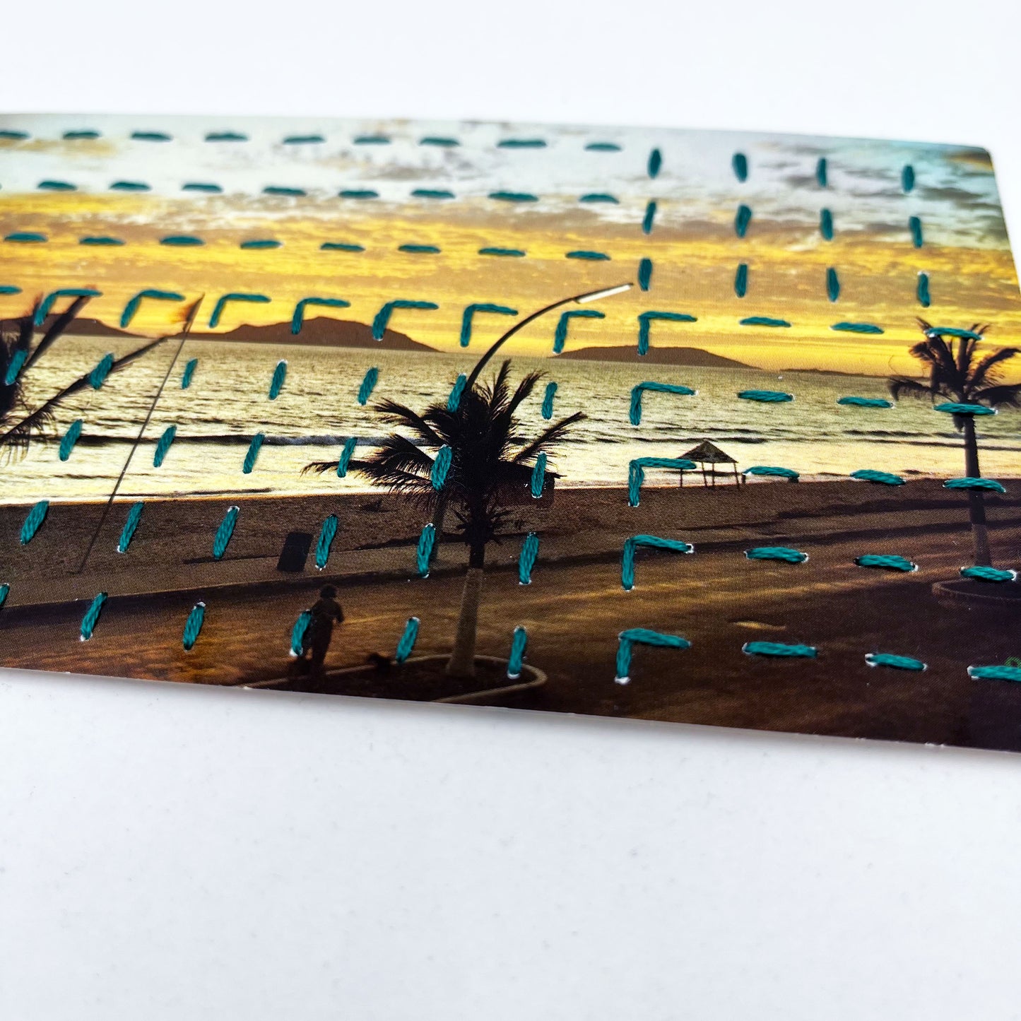 a vintage postcard of a beach sunset in Mazatlan Mexico, hand stitched over with a basketweave running stitch pattern in teal