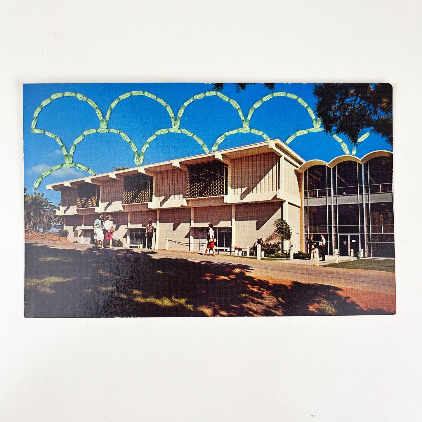 an old postcard of a building at a college in San Diego, with a hand embroidered overlapping circle design like scales in mint green stitched in the background on the sky only, the postcard is sitting on a white background