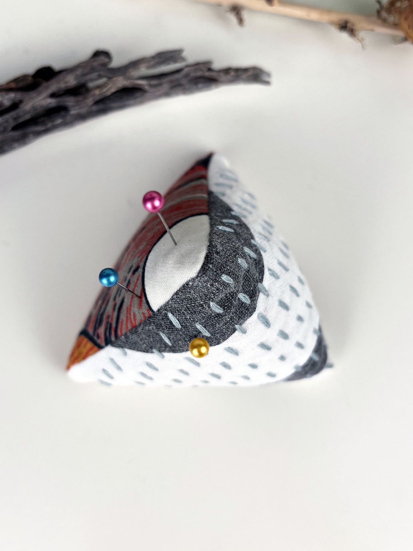 birdseye view of a pyramid pincushion made from floral and black and white fabric with contrasting sashiko stitches on a white counter with dried cholla and seedpods around it