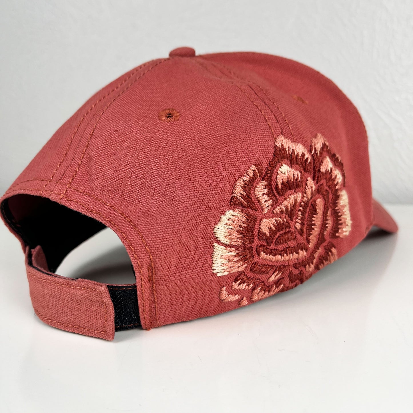 back angled view of a terra cotta colored baseball hat with a large hand embroidered peony on the side, also in shades of terra cotta