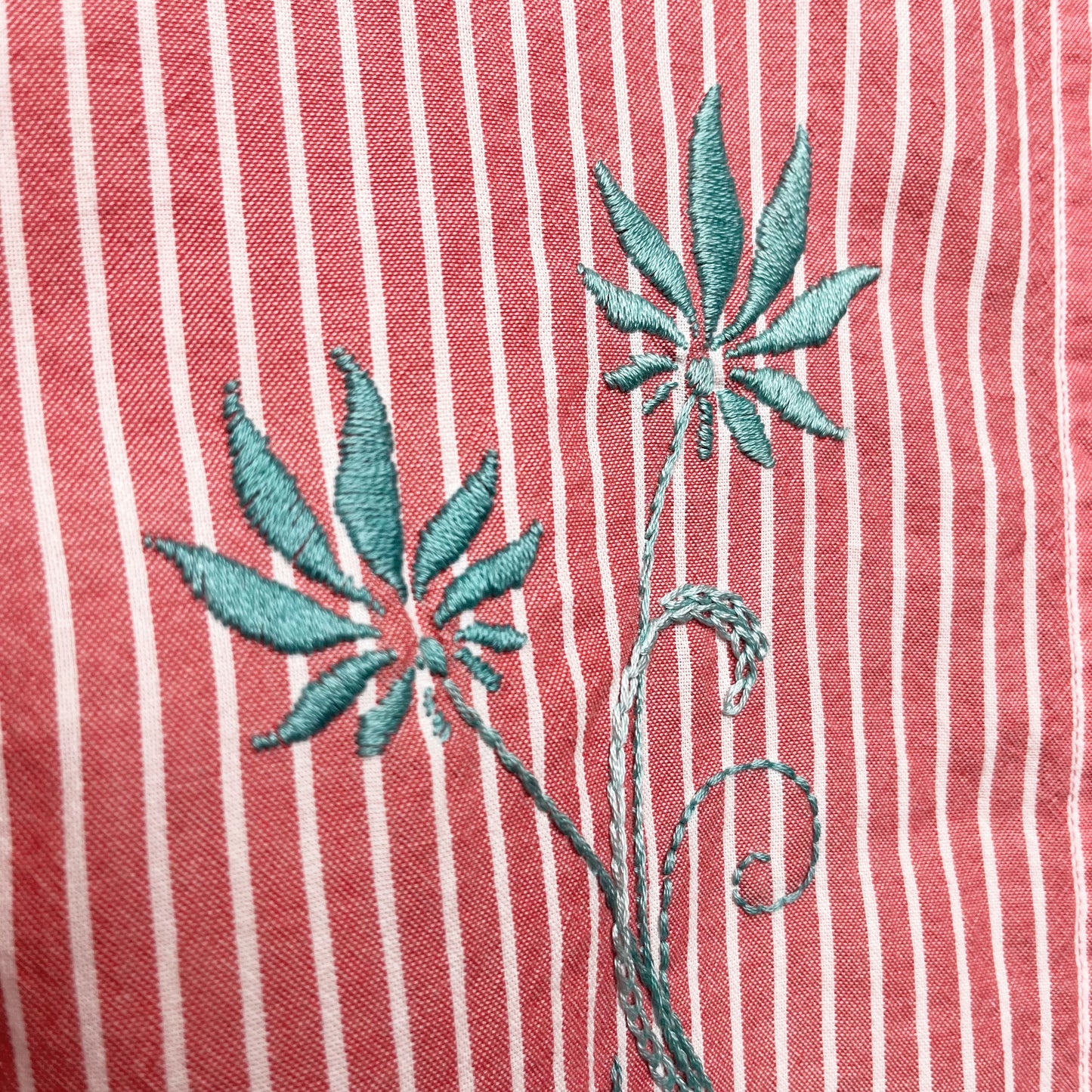 close up of two hand embroidered long stemmed flowers in aqua on a red and white striped button-up short sleeve shirt