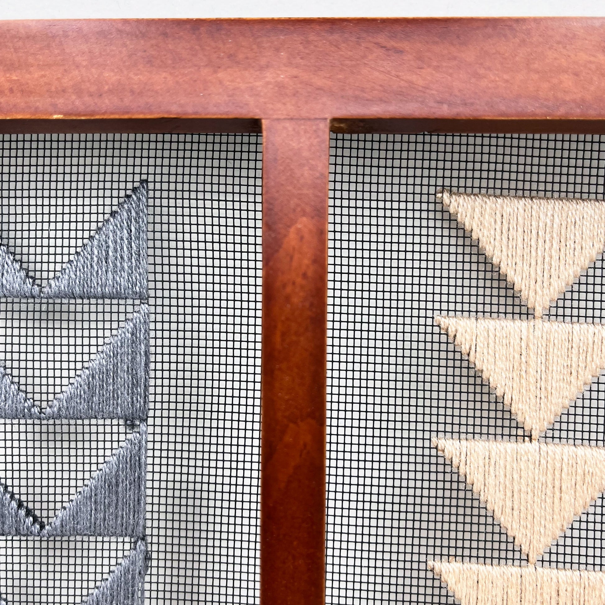 very close up abstract view of Small double panel wood frame holding window screen hand stitched with peach and grey triangles that form shapes of flying geese quilt pattern, on the left side a column of the border triangles in grey, on the right side the center triangles in peach