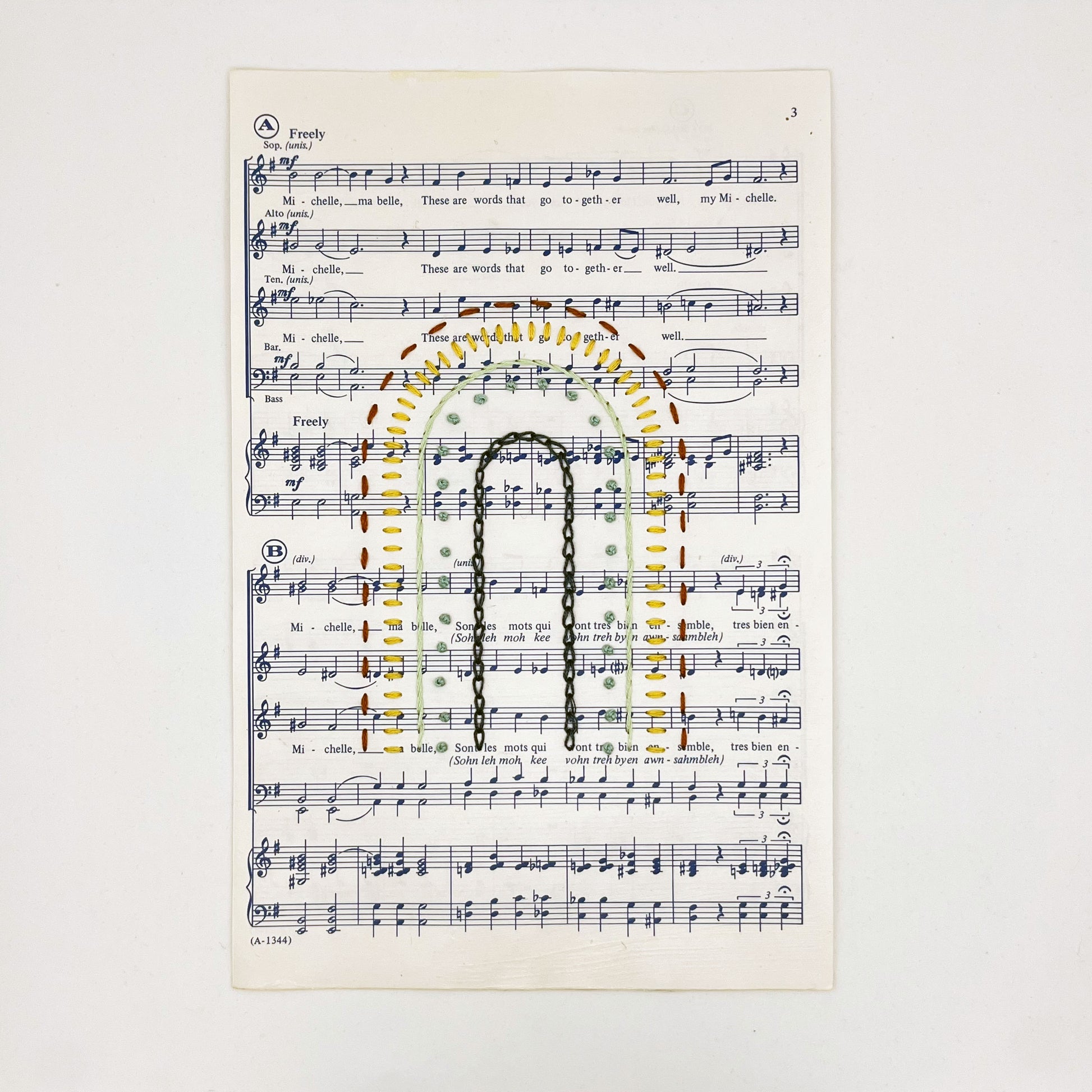 Sheet music for the song "Michelle", hand stitched on in the shape of a rainbow with different types of stitches like chainstitch in dark blue, french knots in green, whipped backstitch in light green, running stitch in red, on a white background