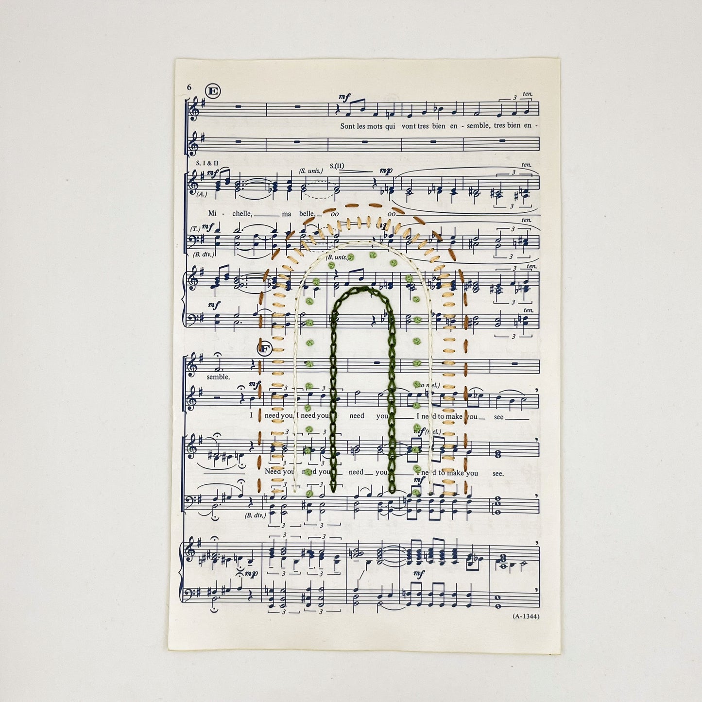 Sheet music for the song "Michelle", hand stitched on in the shape of a rainbow with different types of stitches like chainstitch in dark green, french knots in light green, whipped backstitch in ivory, running stitch in mauve, on a white background