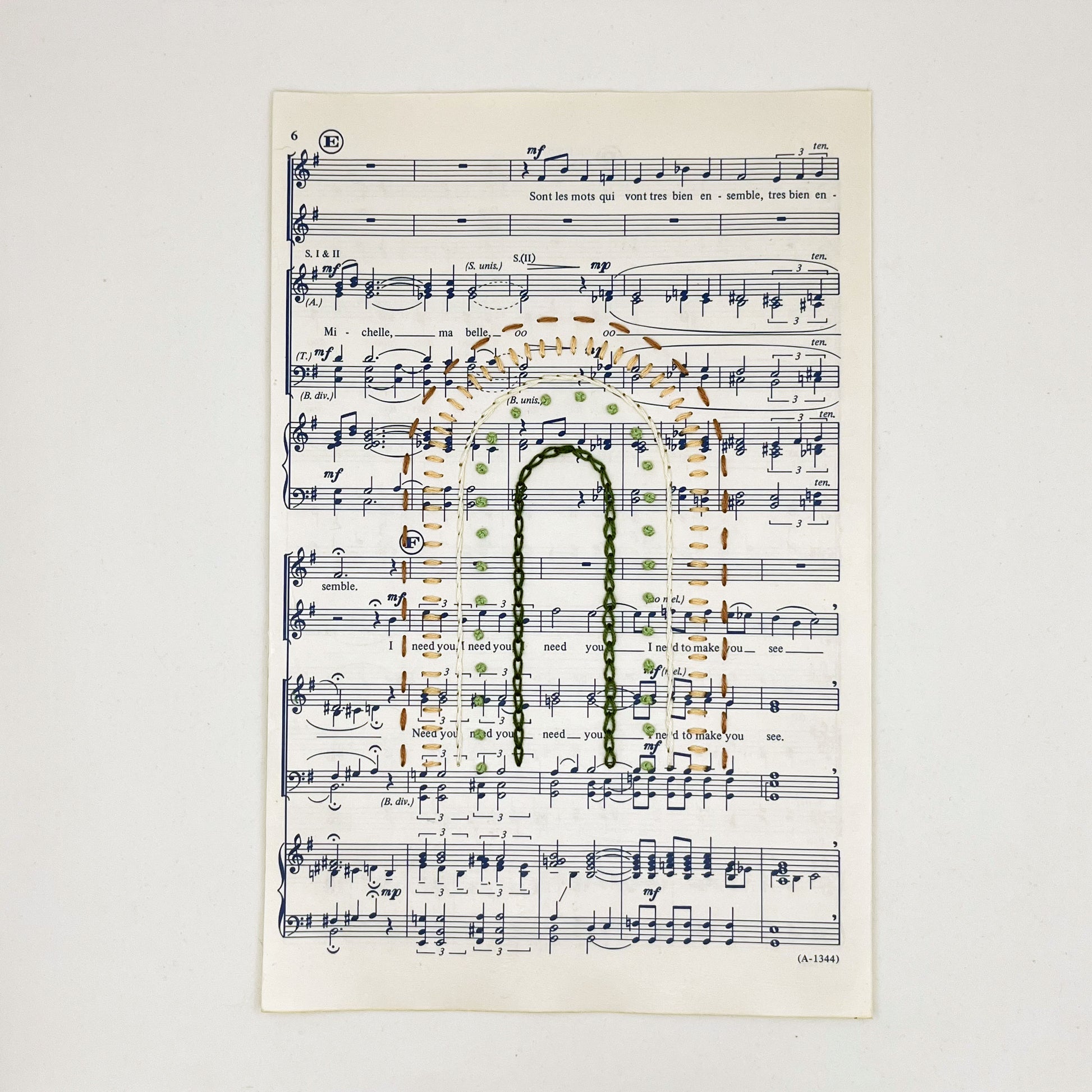 Sheet music for the song "Michelle", hand stitched on in the shape of a rainbow with different types of stitches like chainstitch in dark green, french knots in light green, whipped backstitch in ivory, running stitch in mauve, on a white background