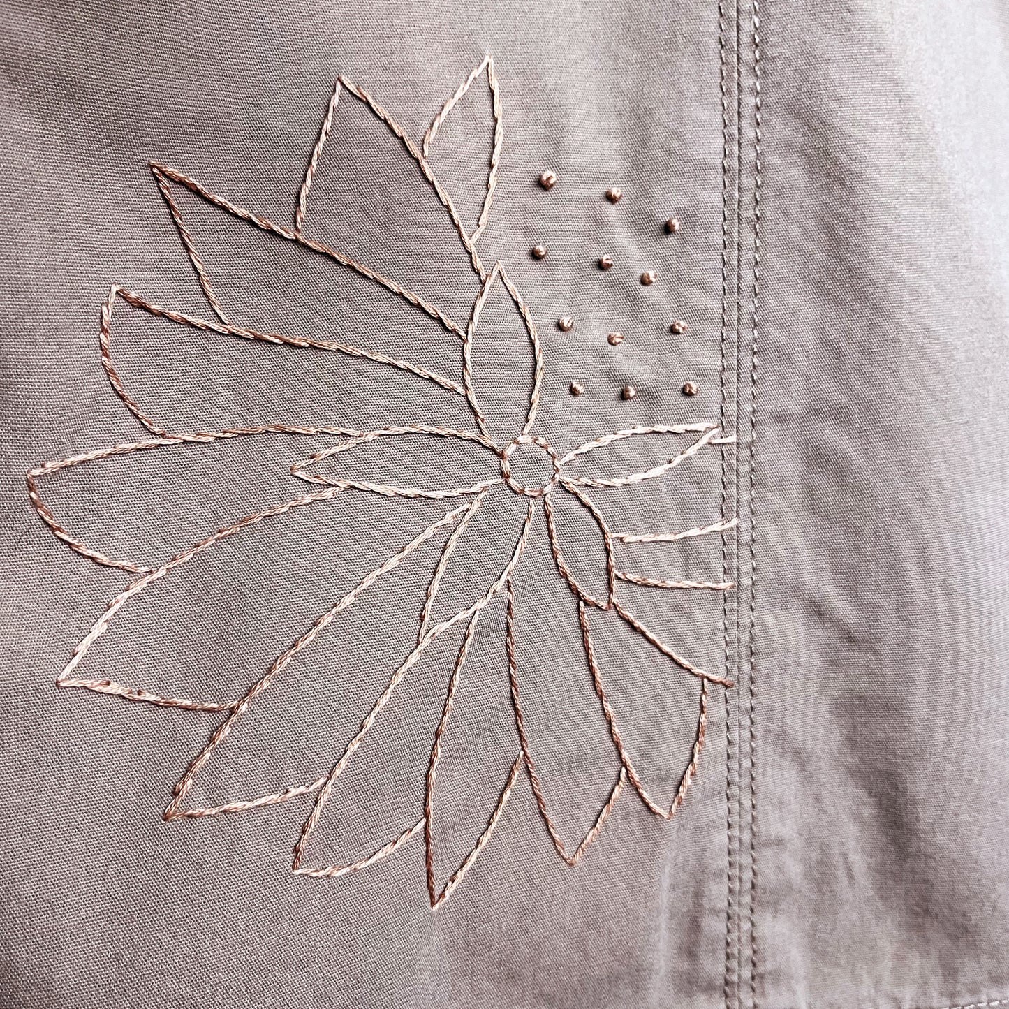 close up view of a hand embroidered outline of an abstract dandelion in the same mauve as the skirt its stitched on