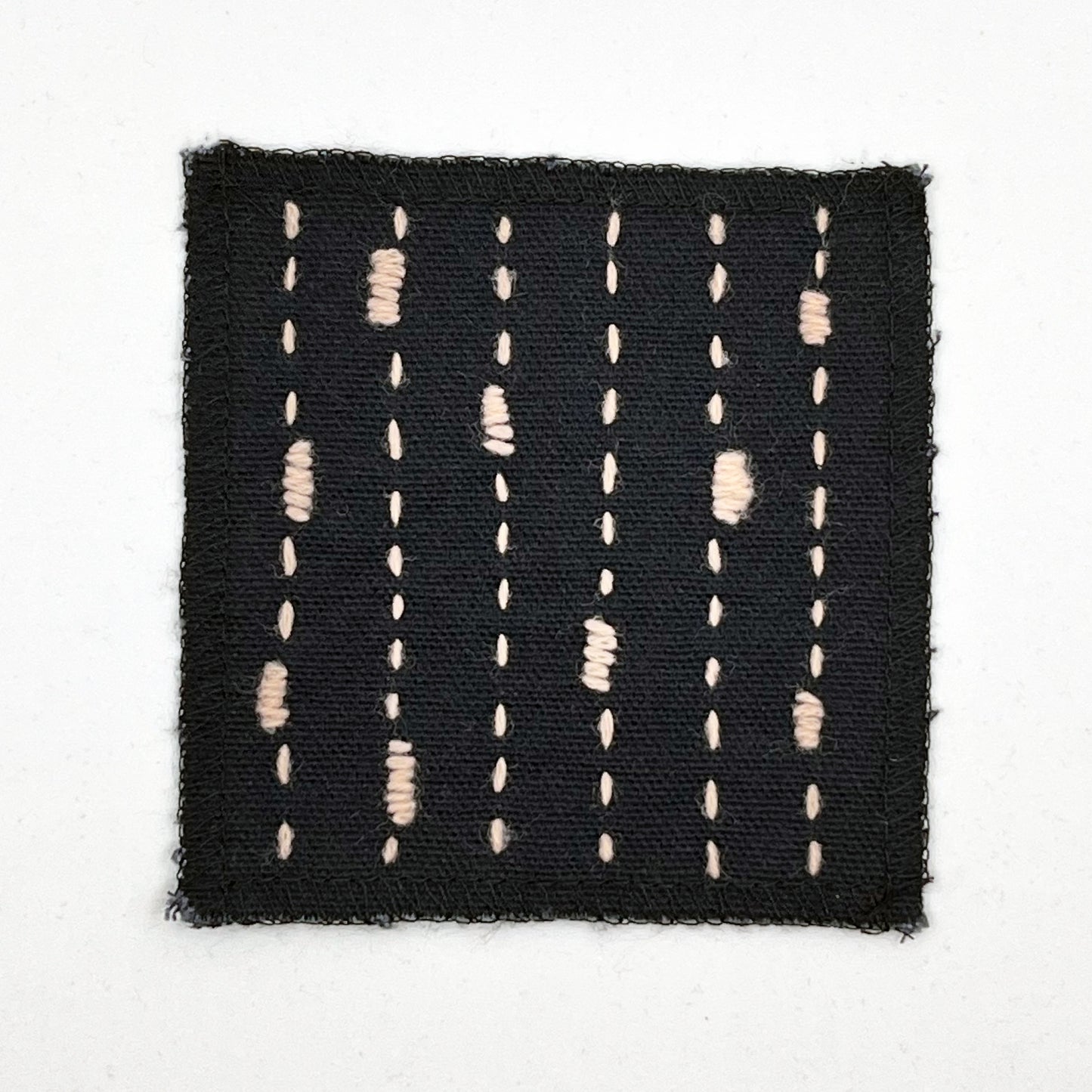 a square patch made out of black canvas, handstitched with peach running stitches with randomly placed small rectangles made of stitches running the other direction, with overlocked edges, on a white background