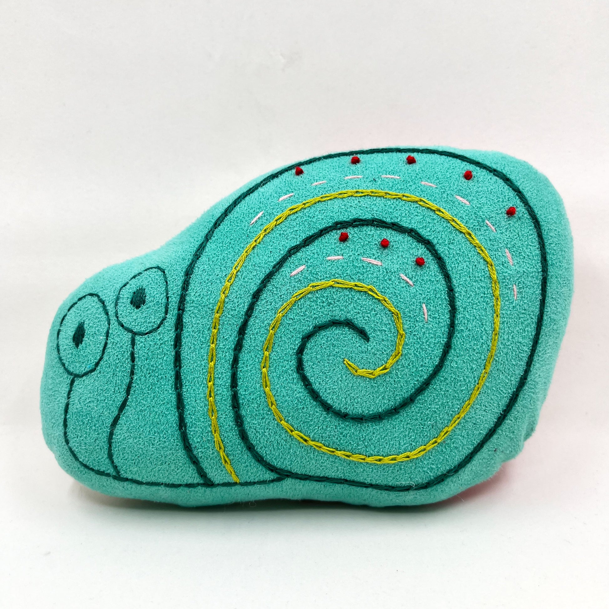 a colorfully hand embroidered stuffed pillow animal of a snail in seafoam green fabric on a white background