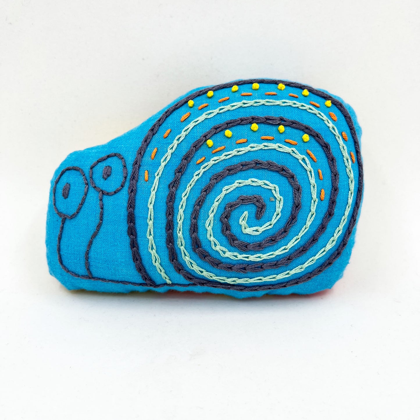 a colorfully hand embroidered stuffed pillow animal of a snail in blue fabric on a white background