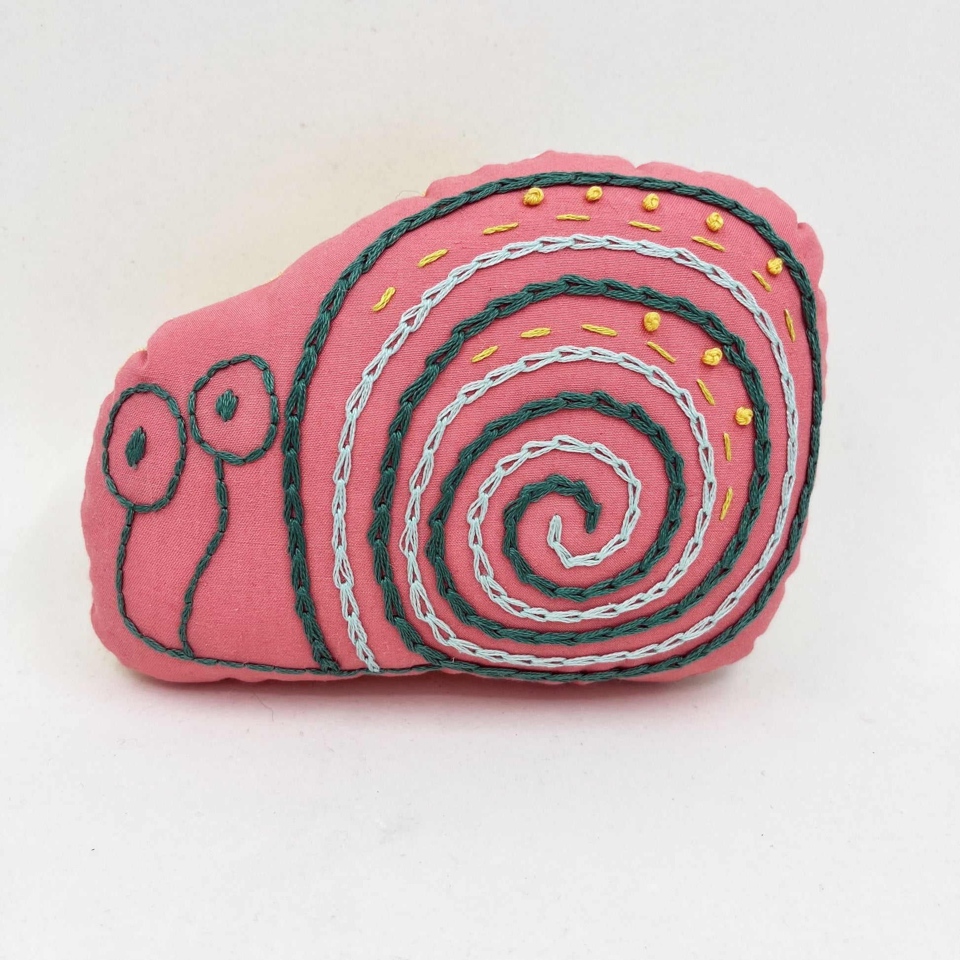 a colorfully hand embroidered stuffed pillow animal of a snail in coral fabric on a white background