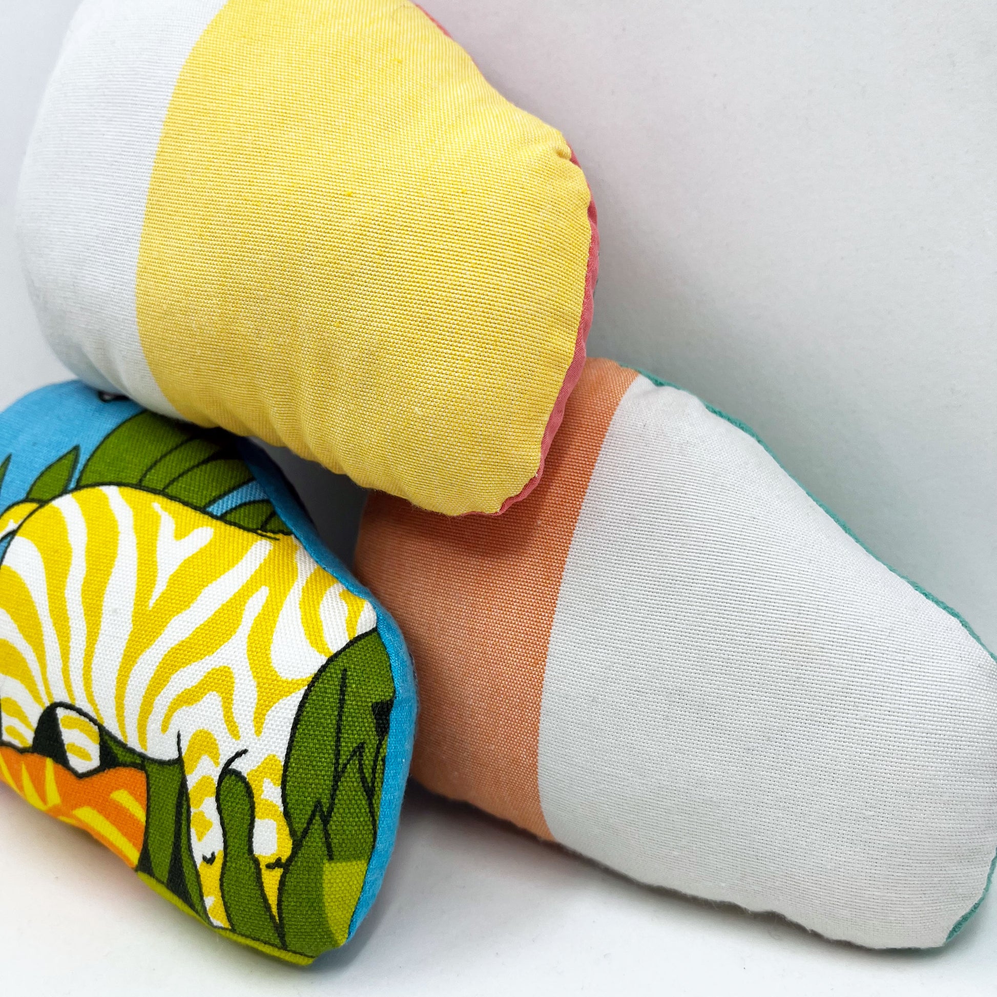 the back sides of a group of colorfully hand embroidered snail stuffed animal pillows in blue, aqua and coral fabric, in a pile on a white background