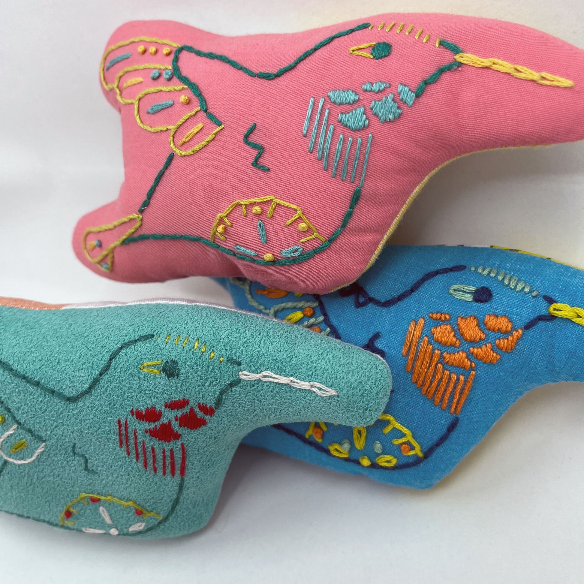 a group of colorfully hand embroidered stuffed pillow hummingbirds in blue, aqua and coral fabric, with a white background