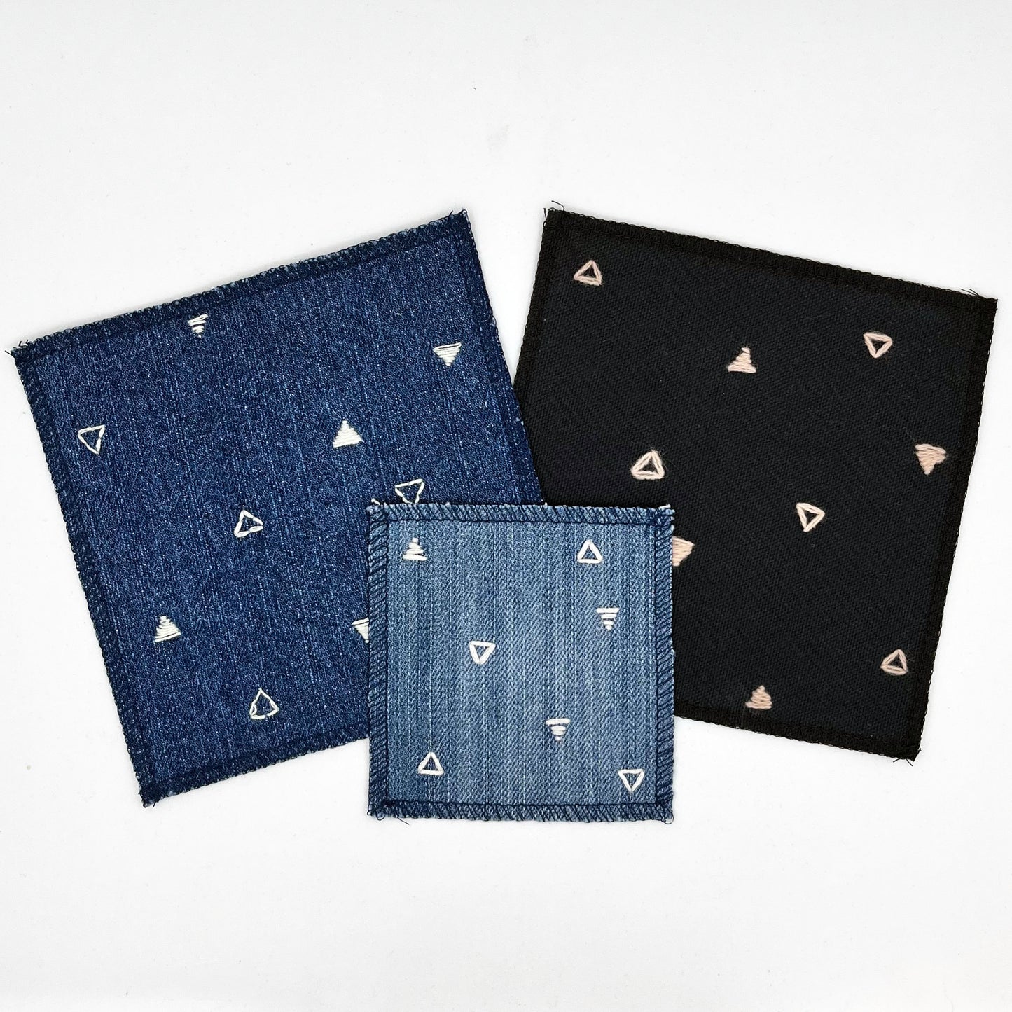 a group of square patches made out of denim and black canvas, hand stitched with scattered ivory or peach triangles, some as outlines some with a line fill, with overlocked edges, on a white background