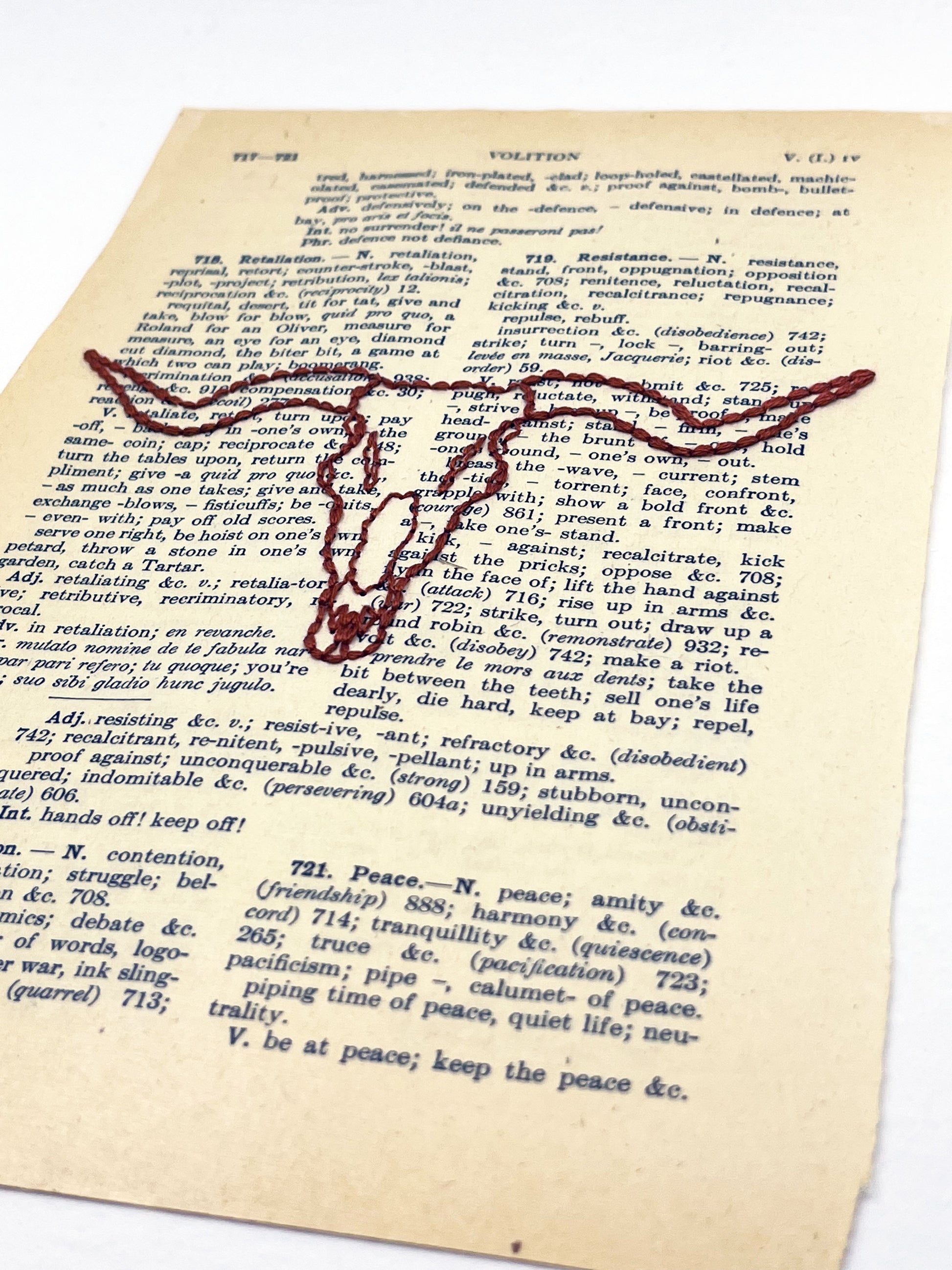 angled view of a vintage thesaurus page hand embroidered in rust colored thread with a longhorn skull on a white background