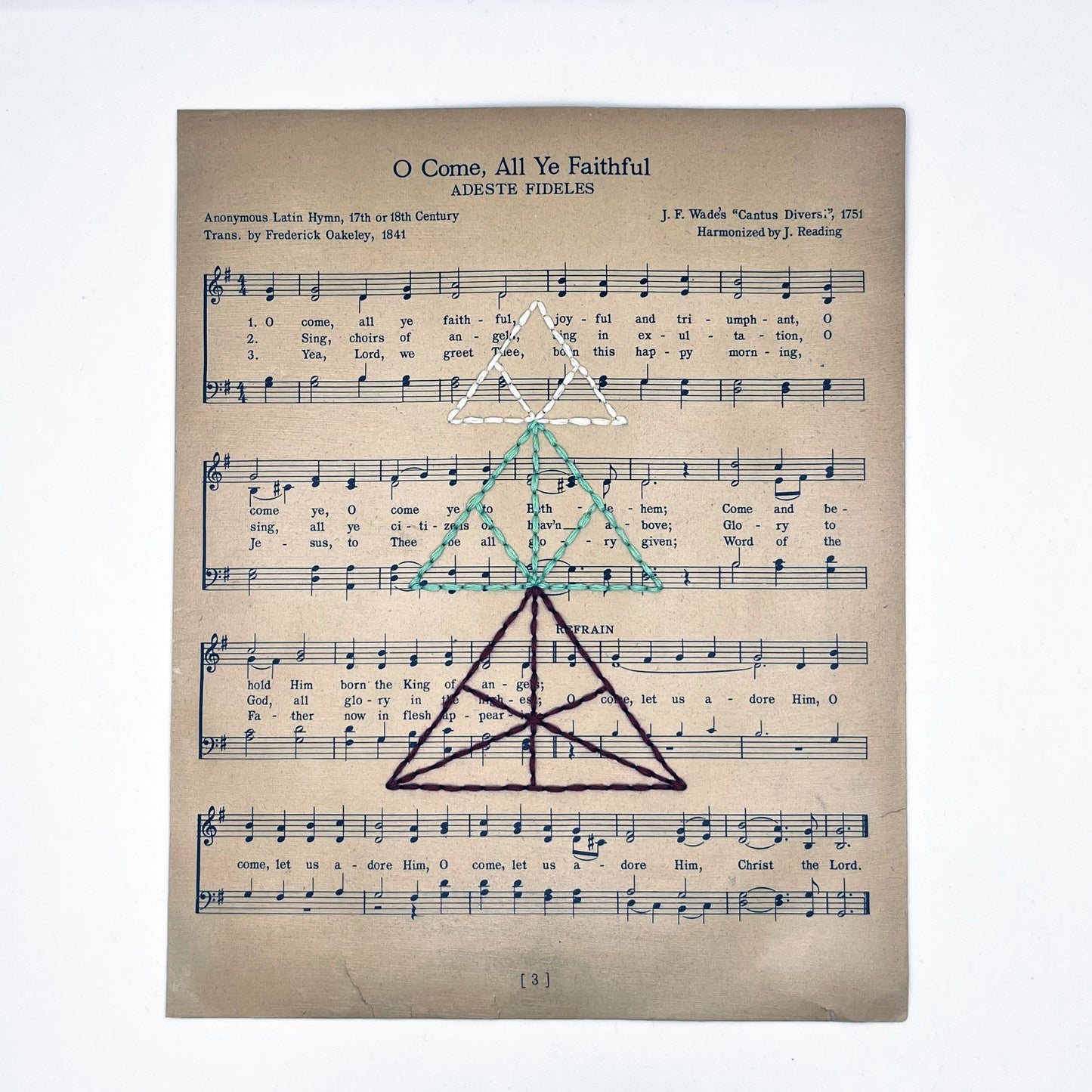 sheet music from the Christmas song O Come All Ye Faithful, hand stitched over with a Christmas tree made from triangles, in red, green and ivory thread